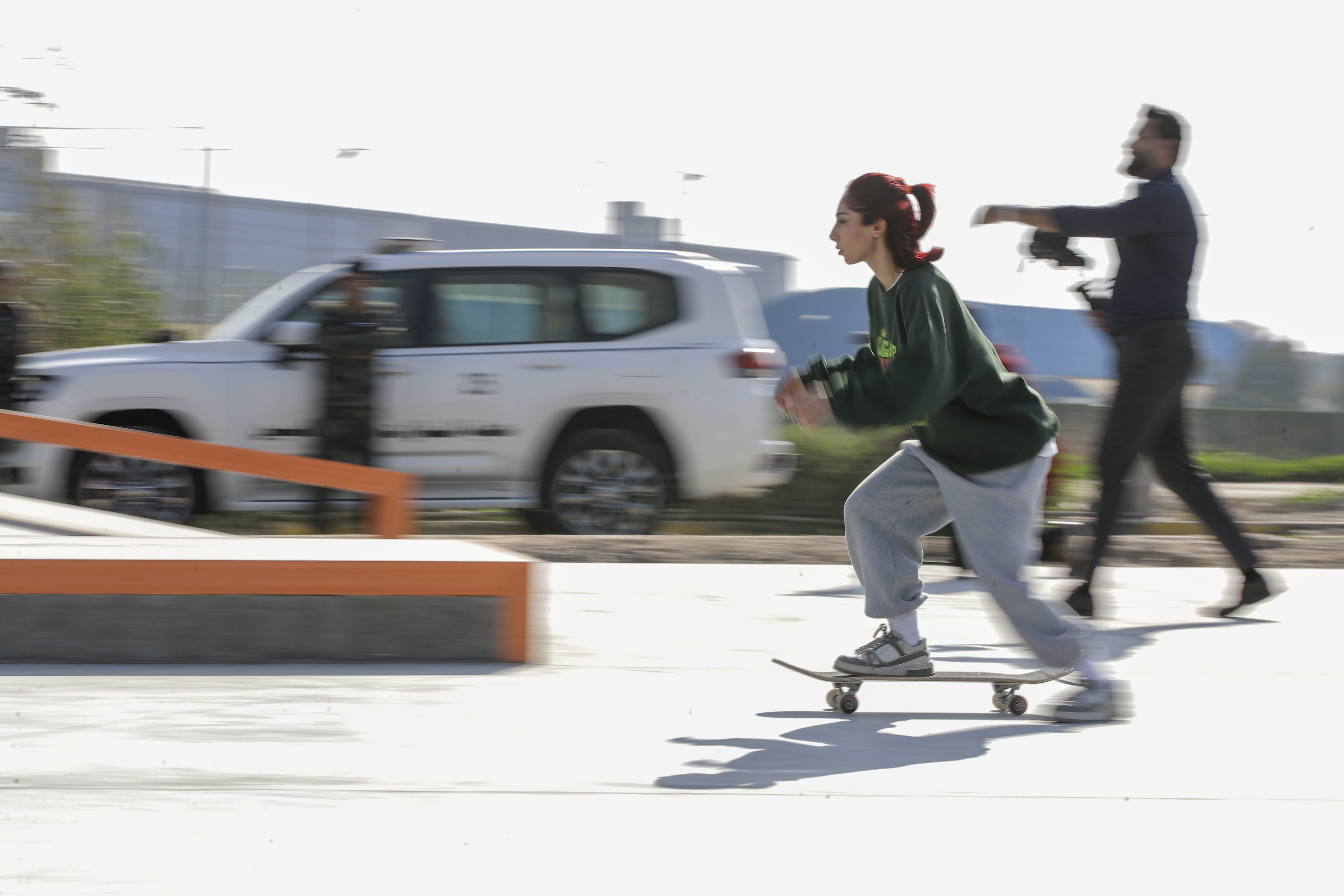 A person on a skateboard riding through an urban setting, with blurred vehicles and pedestrians in the background.