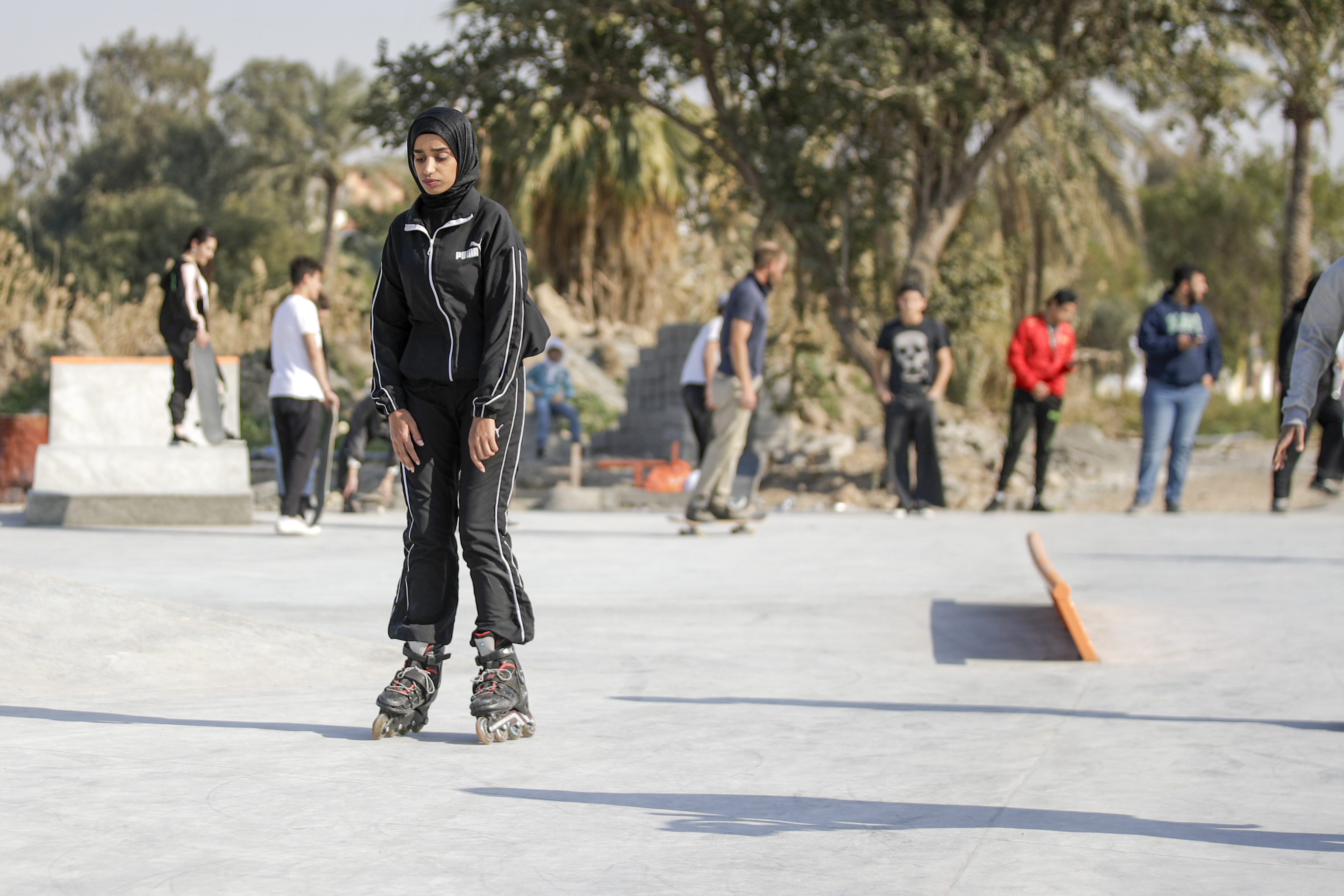Young person in black outfit on rollerskates, outdoors with others in background.