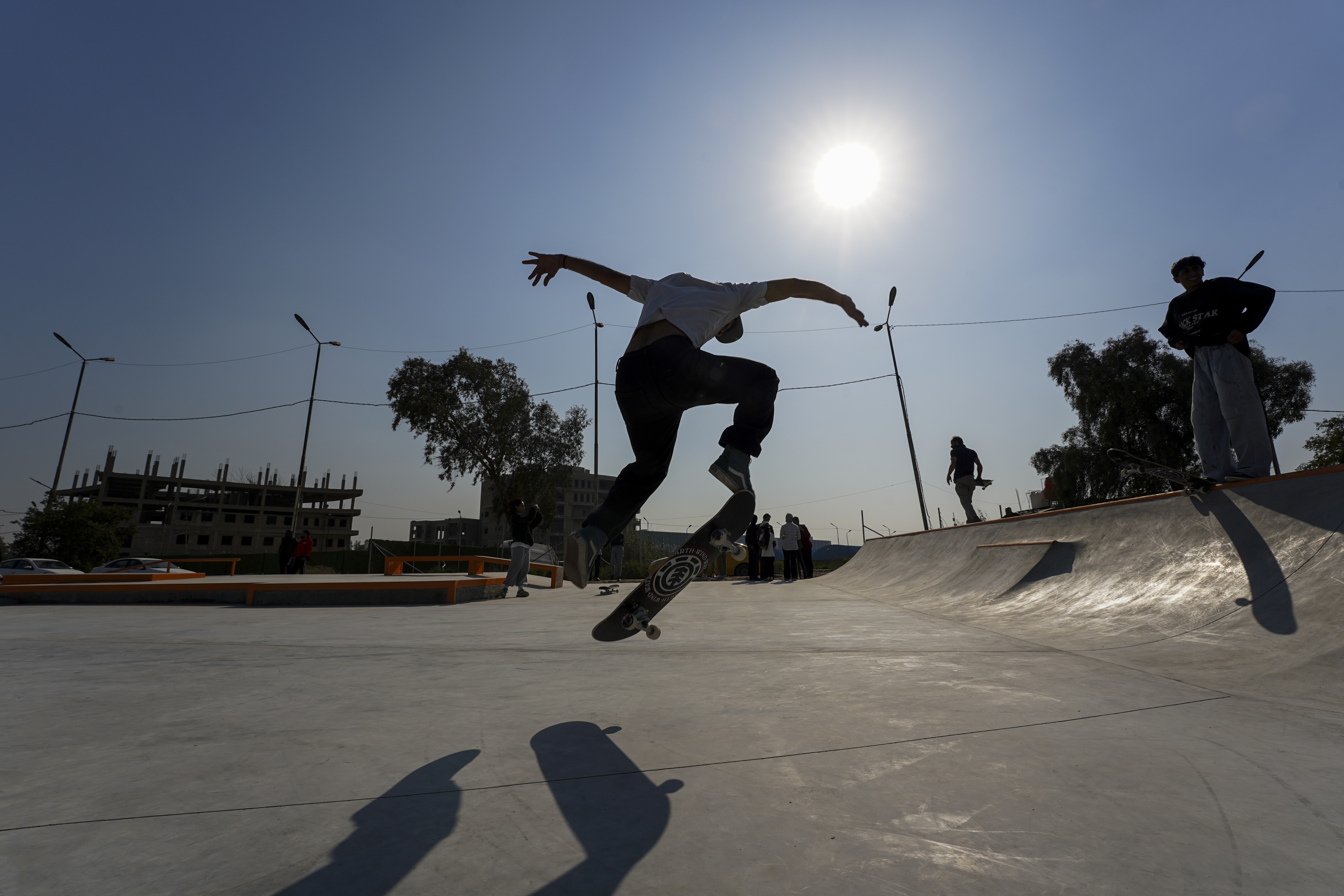 Person performing skateboard trick in skate park, backlit by sunlight.