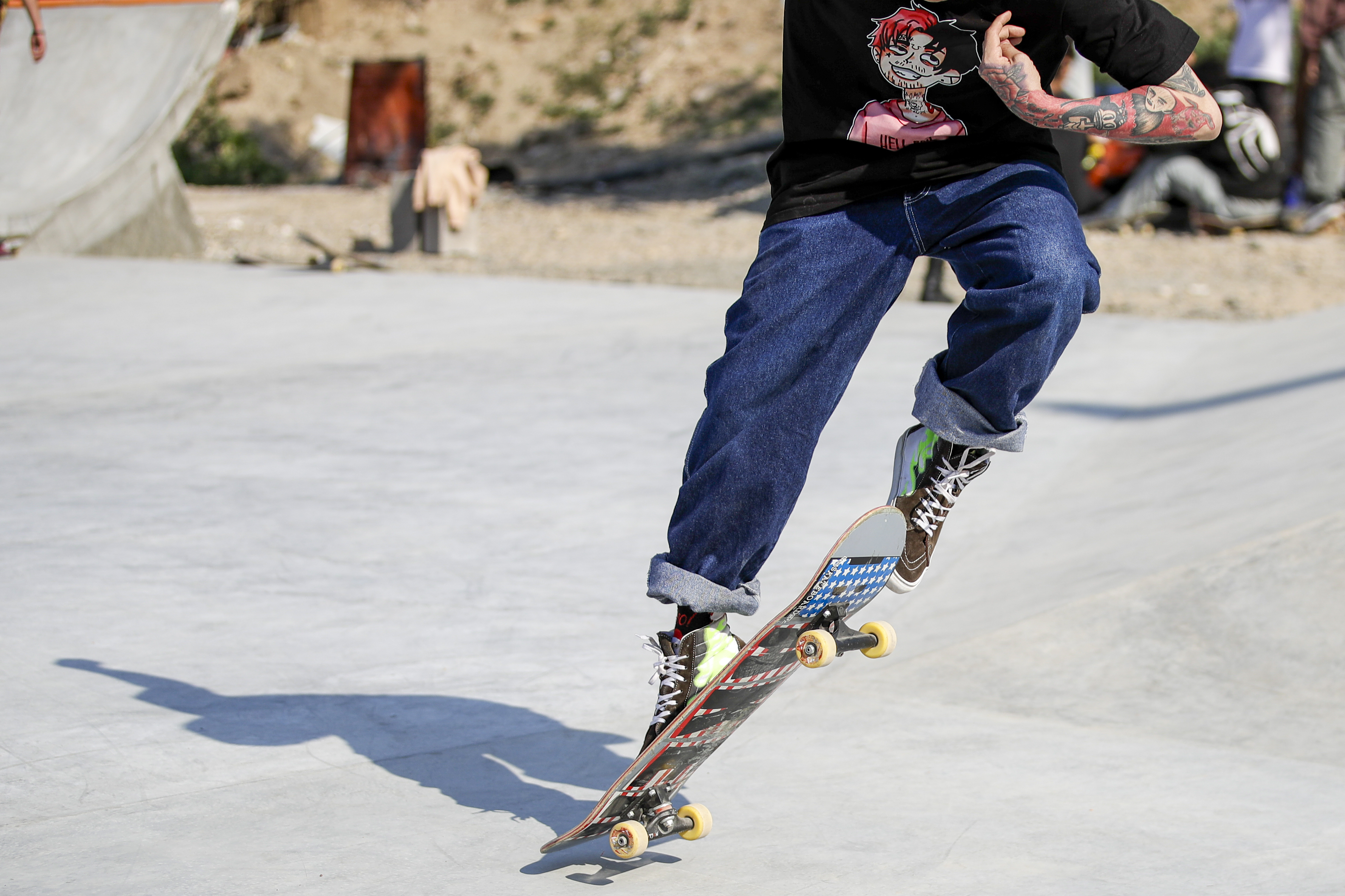 Person wearing black shirt and blue jeans riding a skateboard on a concrete surface.
