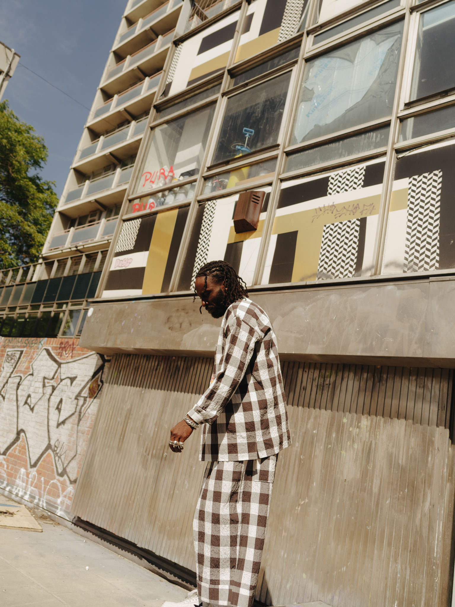 Person in chequered brown and white outfit walking past concrete building with geometric patterned windows and balconies.