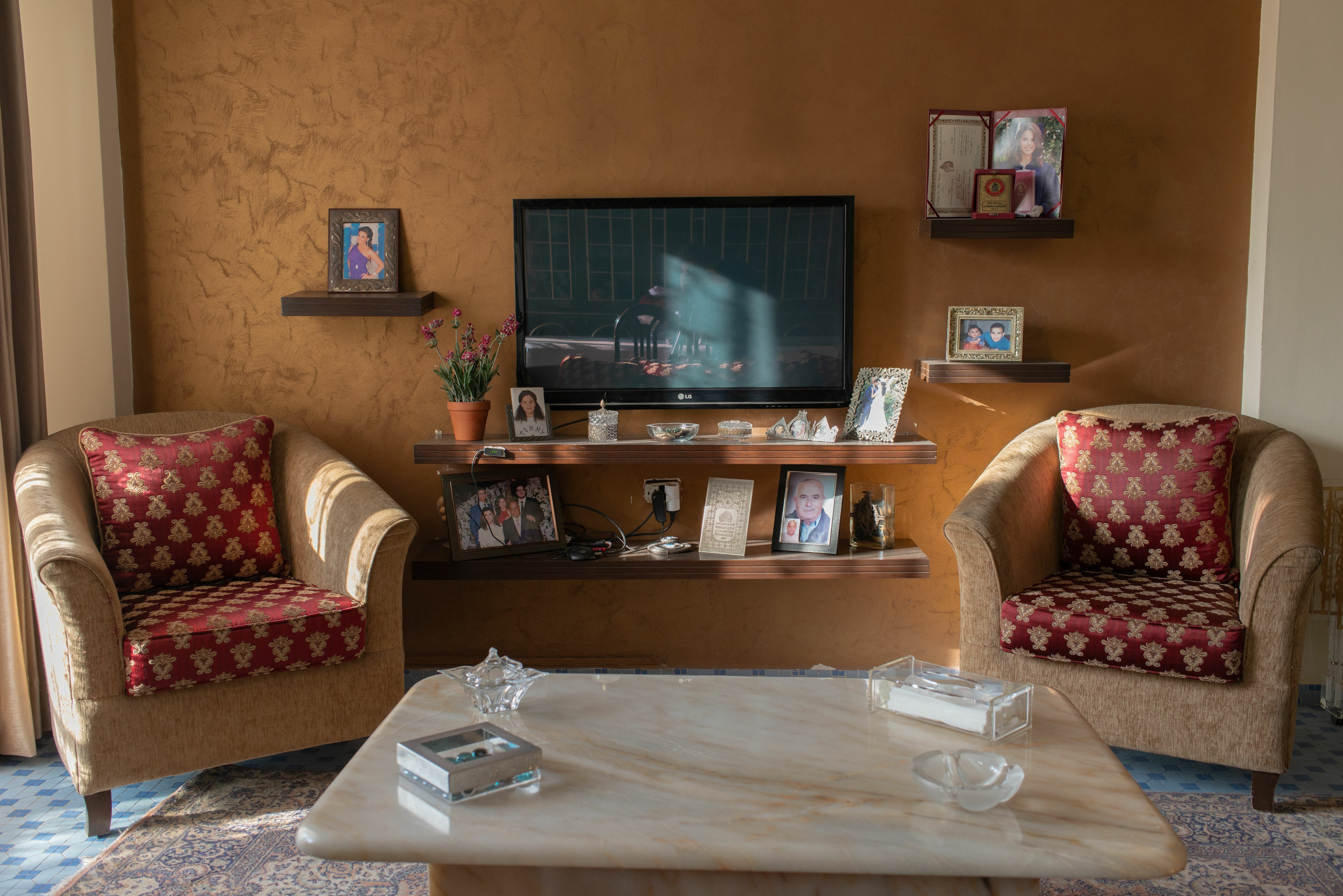 Cosy living room with patterned chairs, shelving unit with photos, and a large wall-mounted TV.
