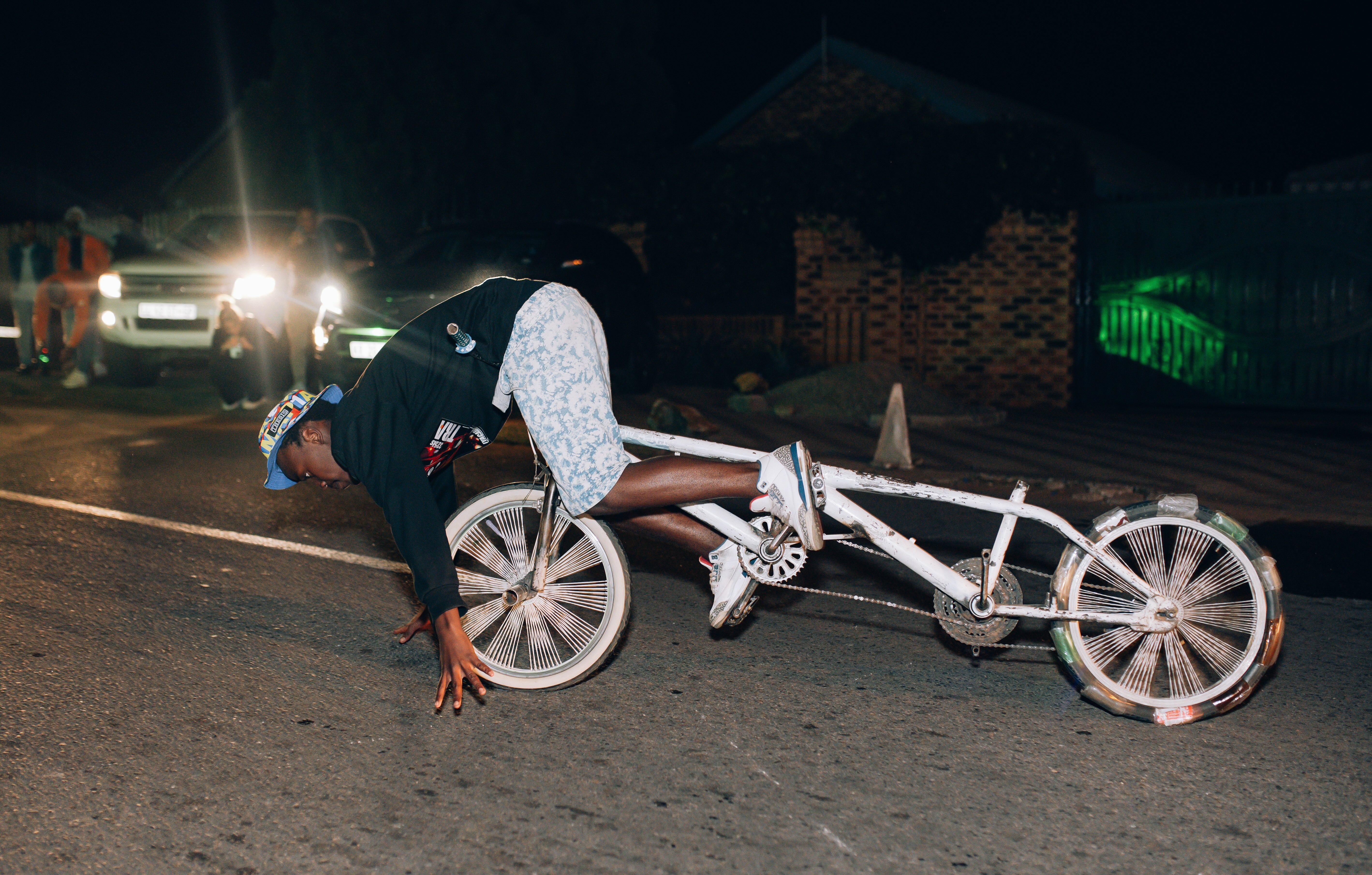 A person riding a bicycle with distinctive handlebars and wheels in a night-time urban setting.