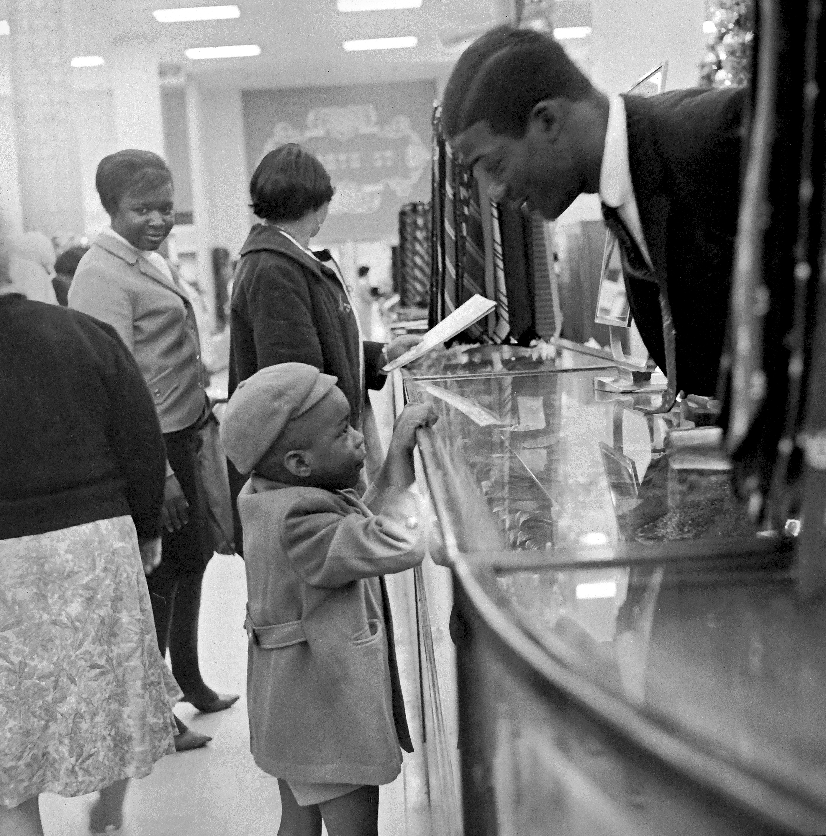 Several people, some children, gathered around a glass display case in a room. A man is leaning over the display case, examining it closely.