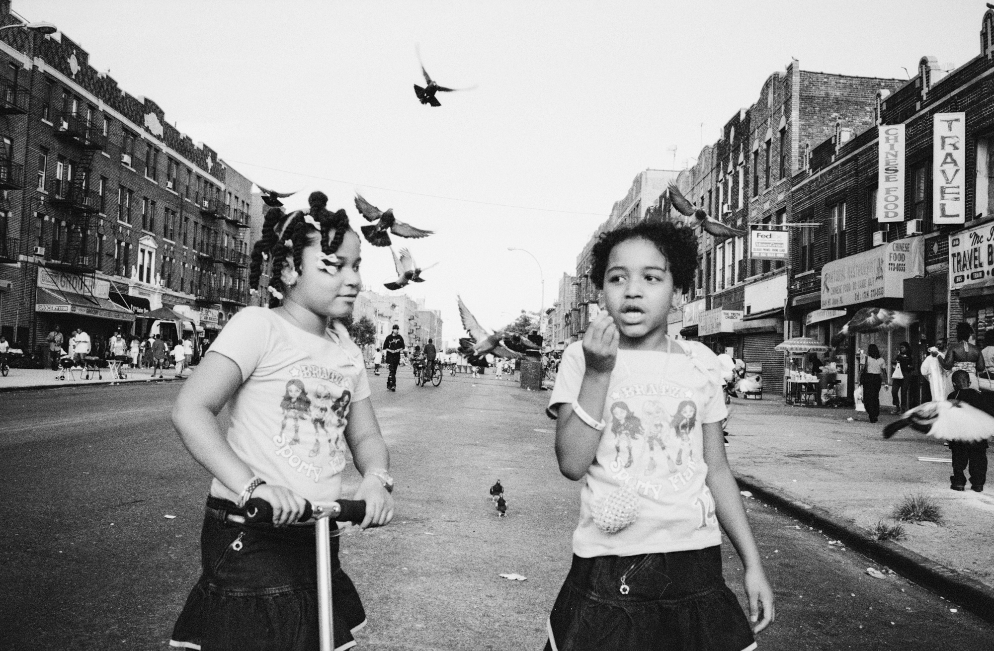 Two young children standing on a busy urban street, with a low-flying helicopter and birds overhead.