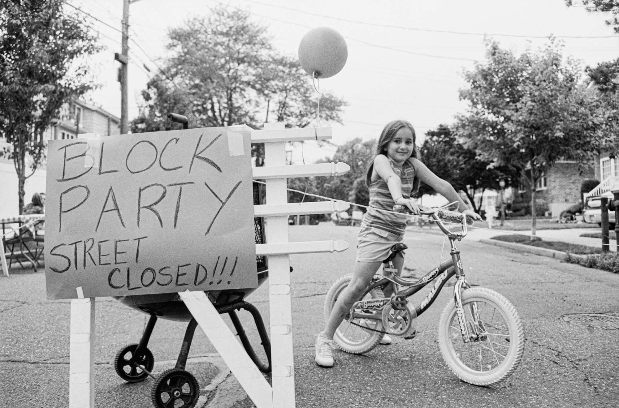 A young girl riding a bicycle on a street with a sign that says "Block Party Street Closed!!!"