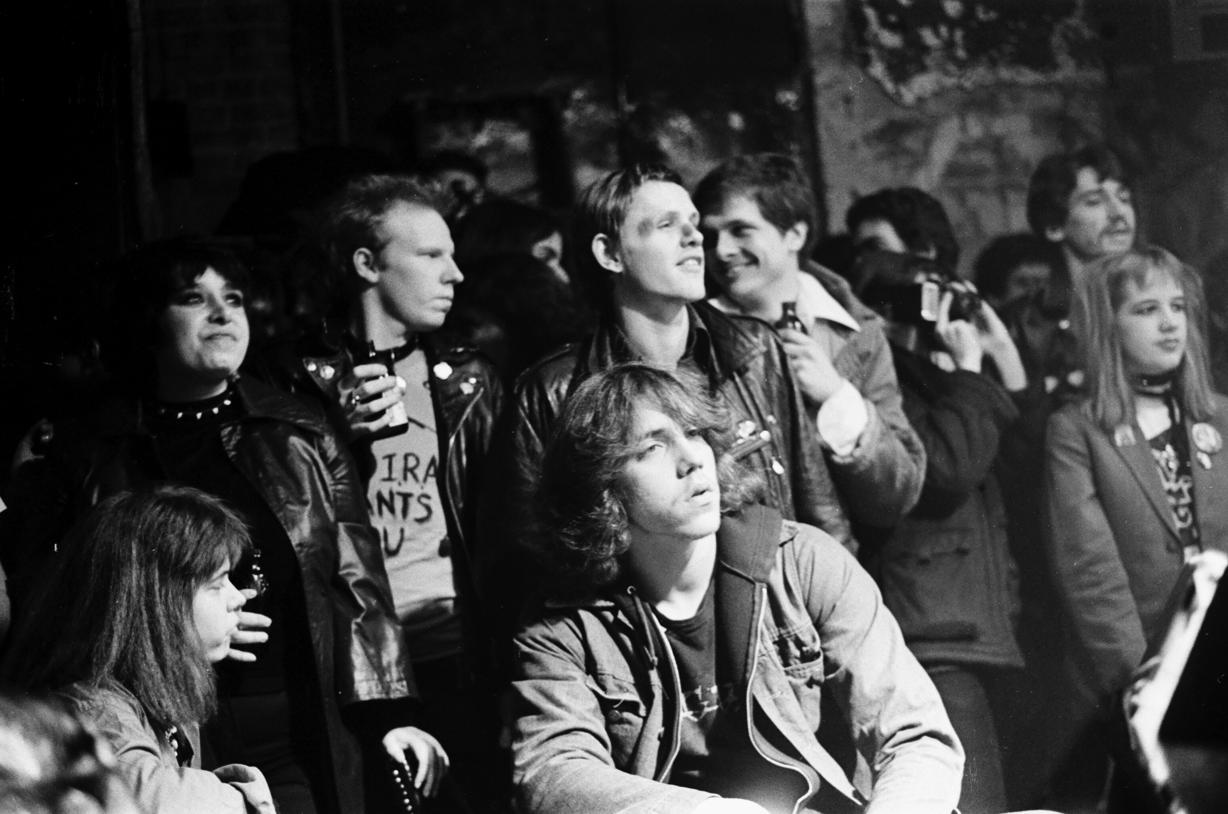 Black and white image of a group of young people, some wearing punk or alternative fashion, gathered together outdoors.