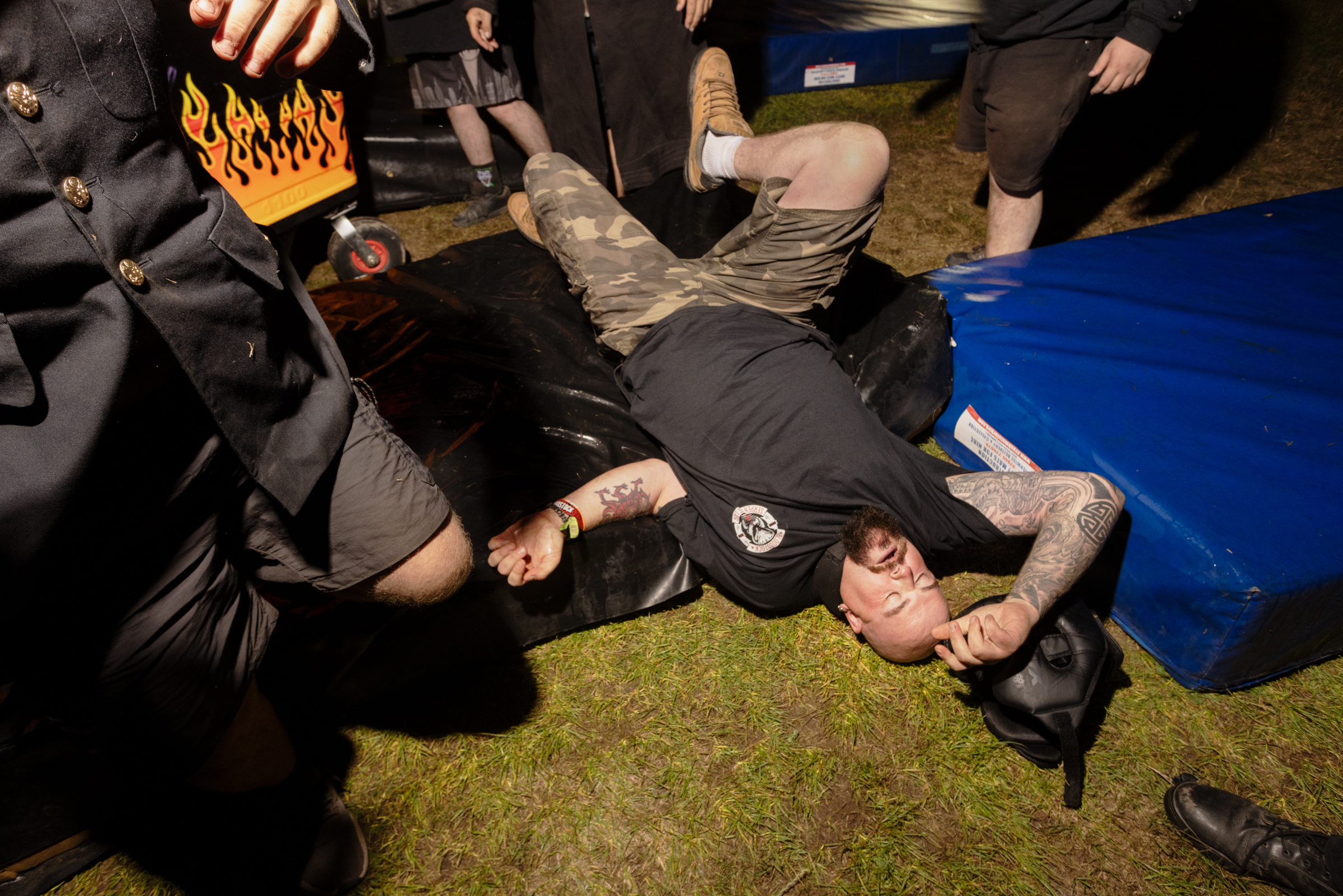 Police officers restraining a person on the ground during an arrest, with onlookers nearby on grass surface at night.
