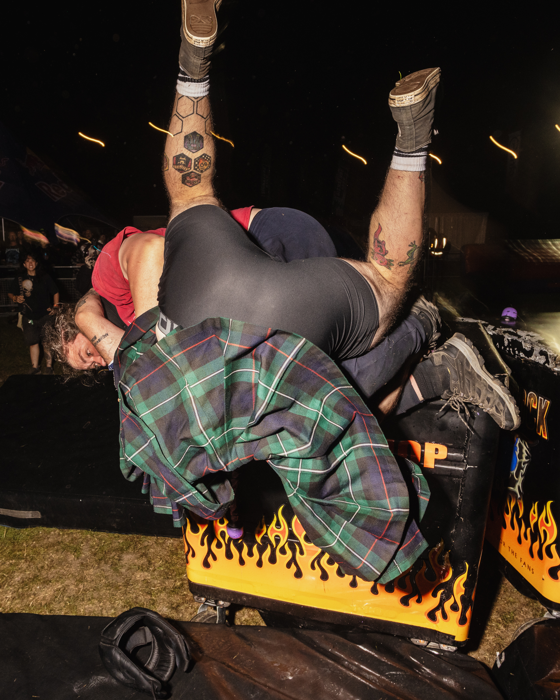 Person with tattooed legs in grey leggings and plaid flannel shirt performing headstand on yellow platform with flame design.
