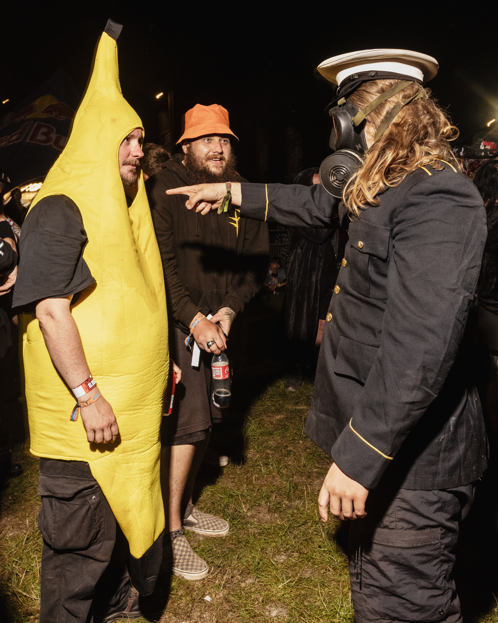 Three people in fancy dress costumes: yellow banana suit, orange bucket hat with dark clothing, and naval uniform with cap and gas mask.