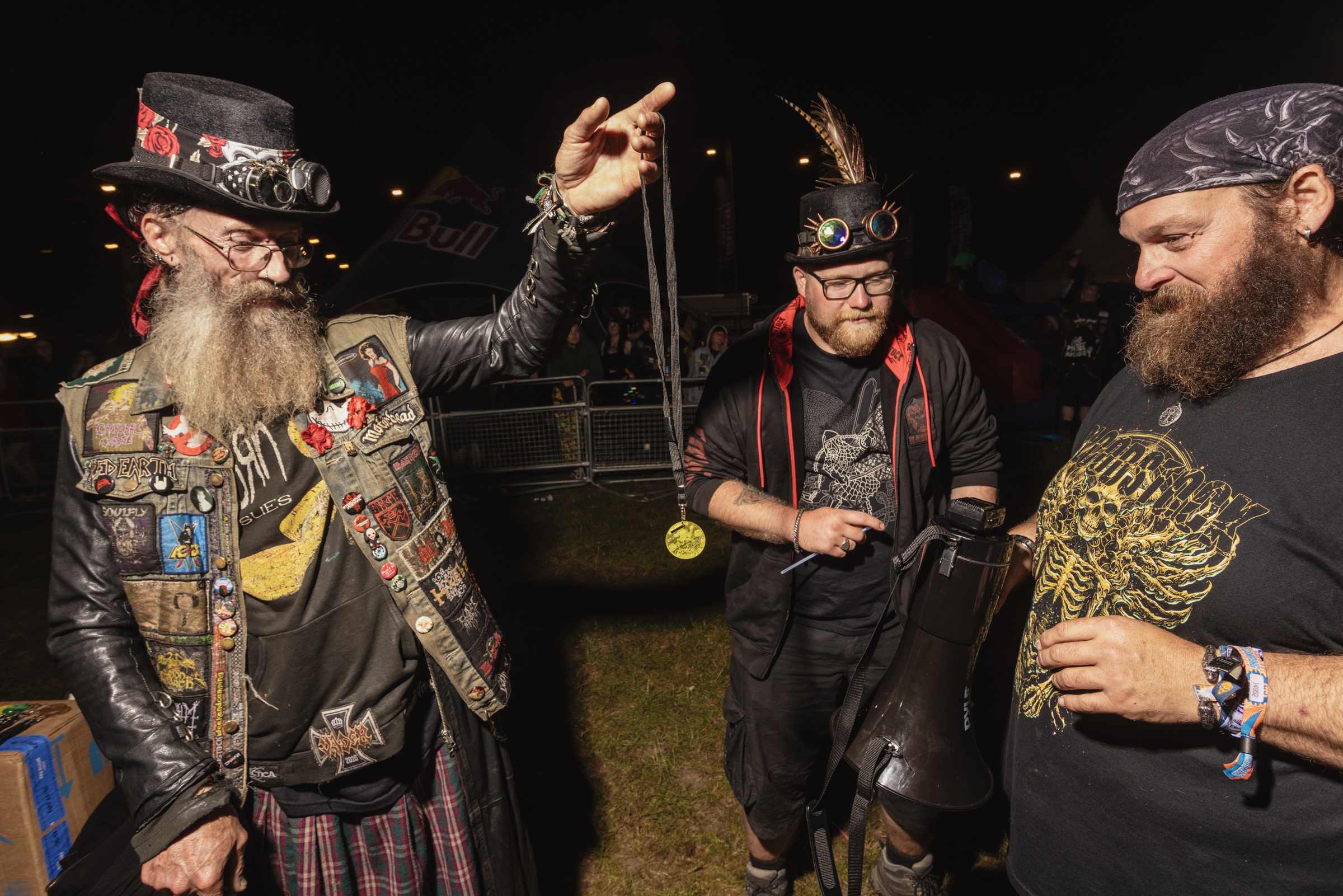 Four bearded men in steampunk costumes with goggles, patches, and accessories standing together at night event.
