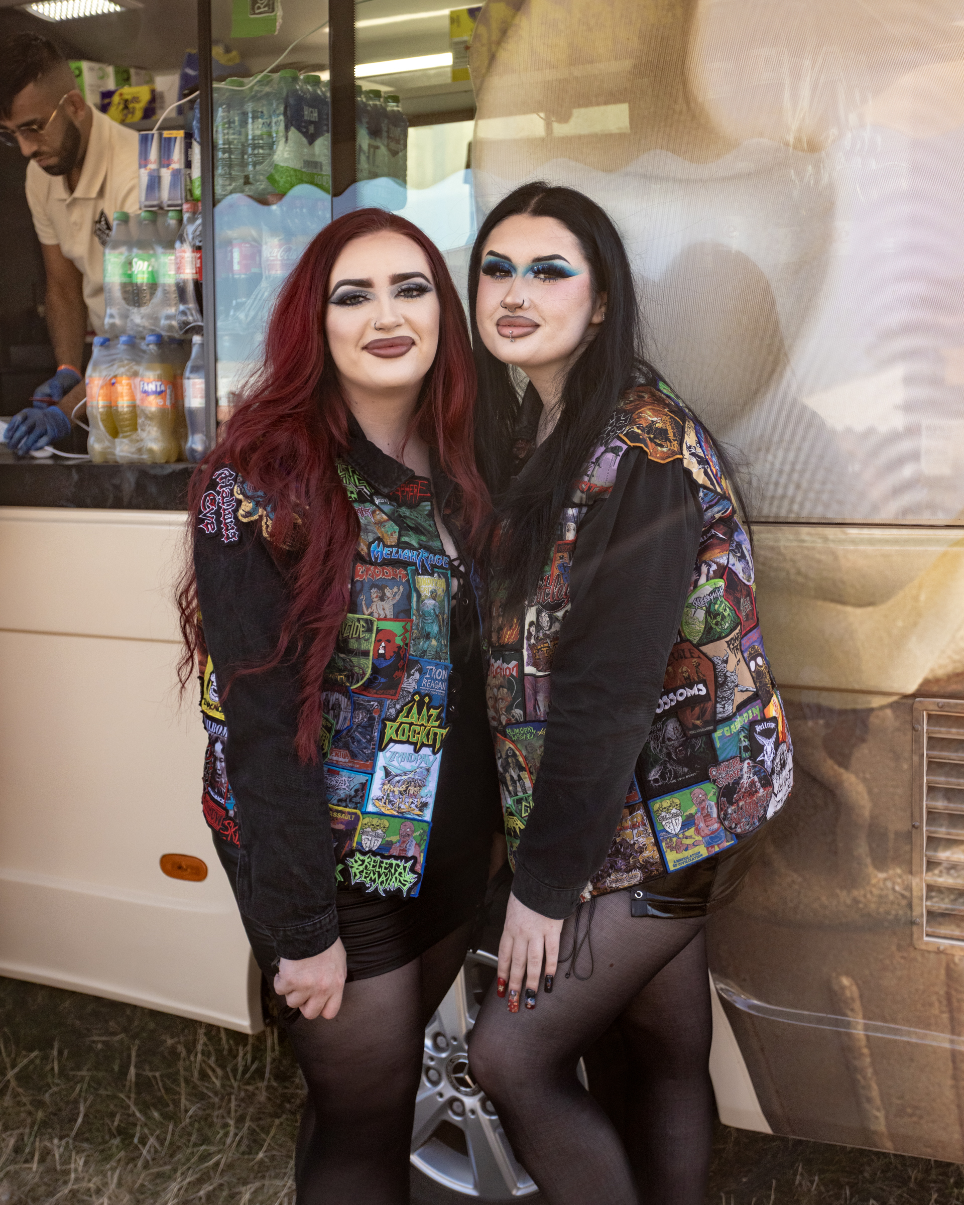 Two women with long dark hair wearing matching colourful patchwork jackets with comic-style graphics, posing together indoors.