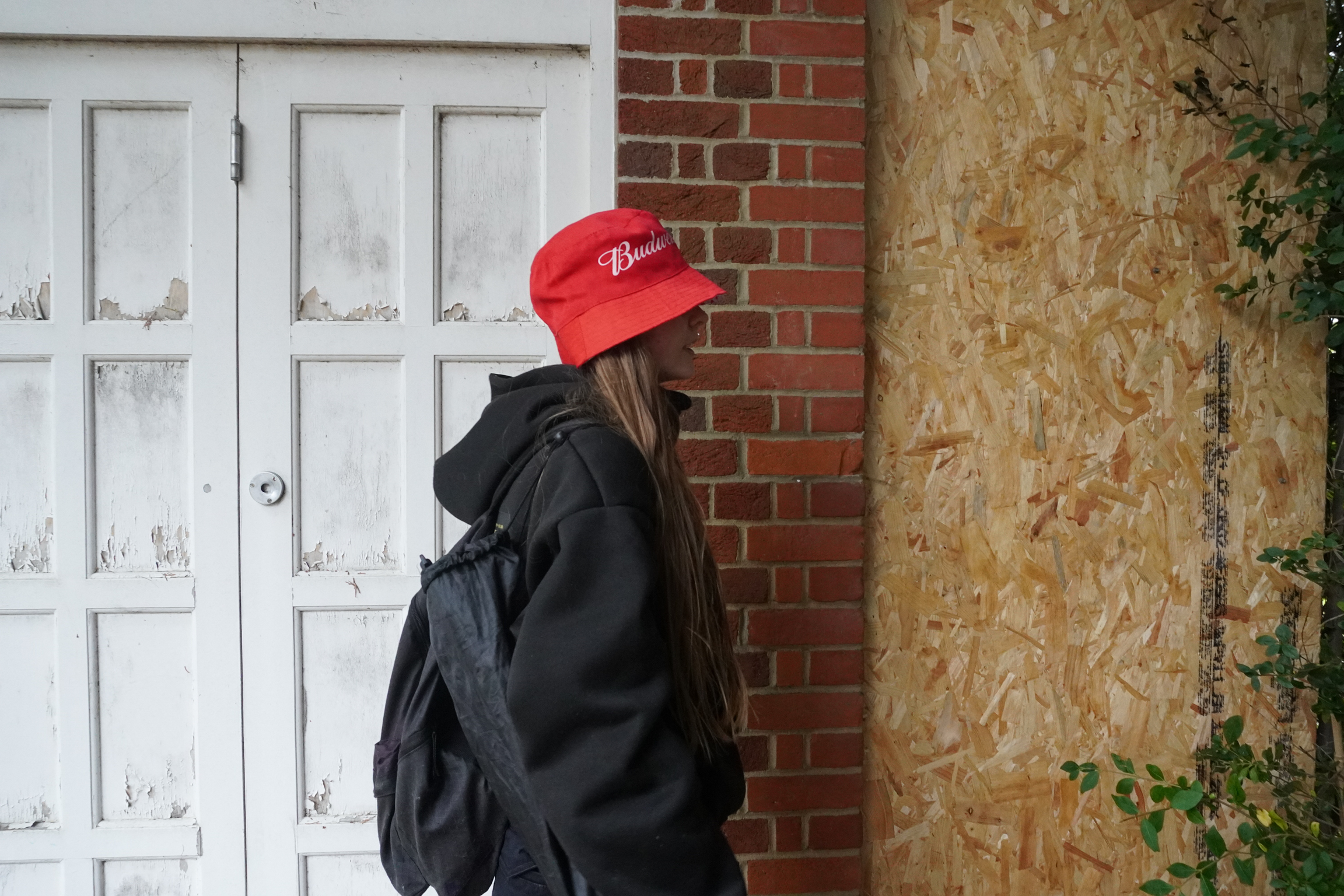 Person in black jacket and red cap standing near white wooden doors and red brick wall with stone surface visible.