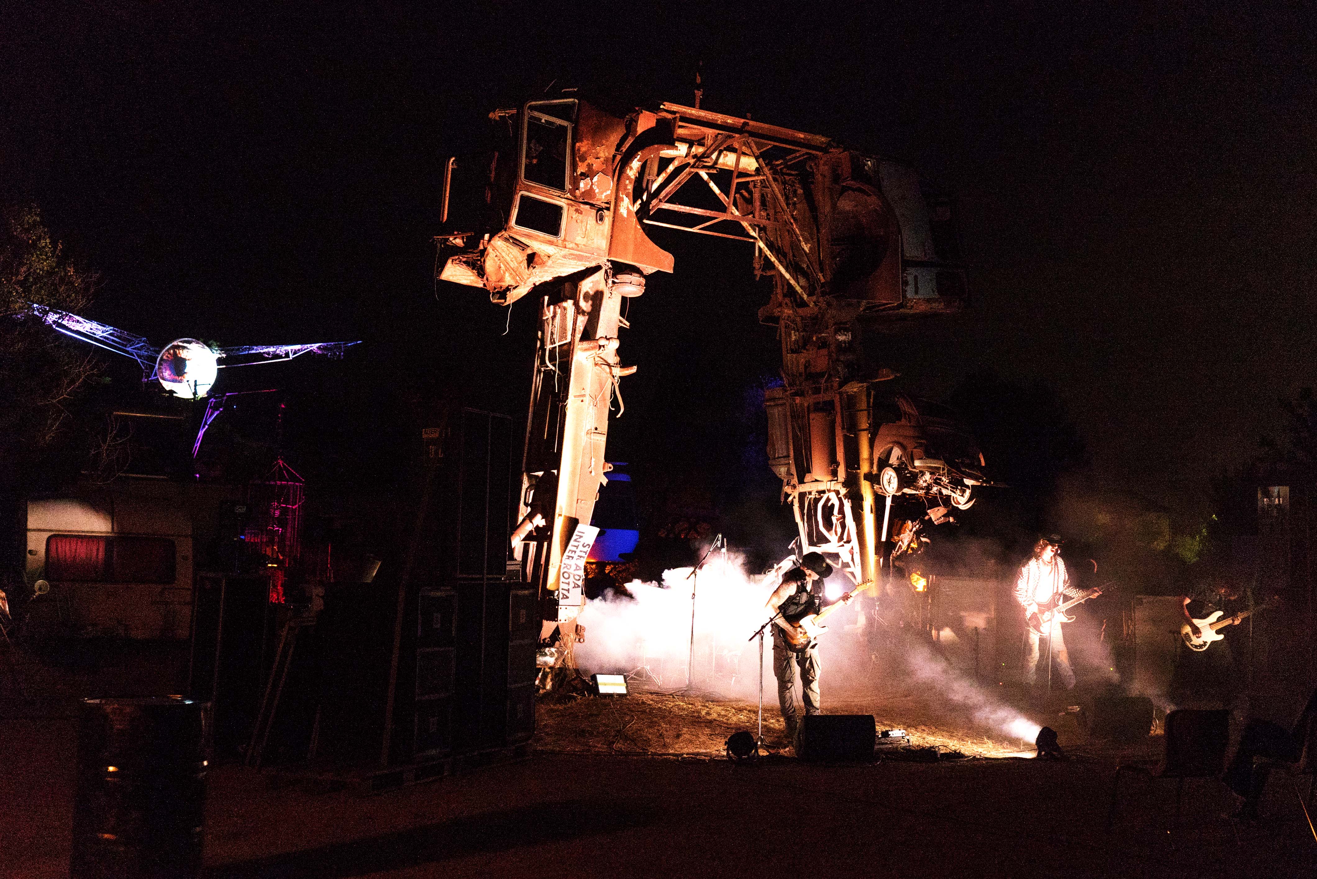 Large mechanical walker robot with orange lighting and steam effects on dark stage, with smaller flying drone nearby.