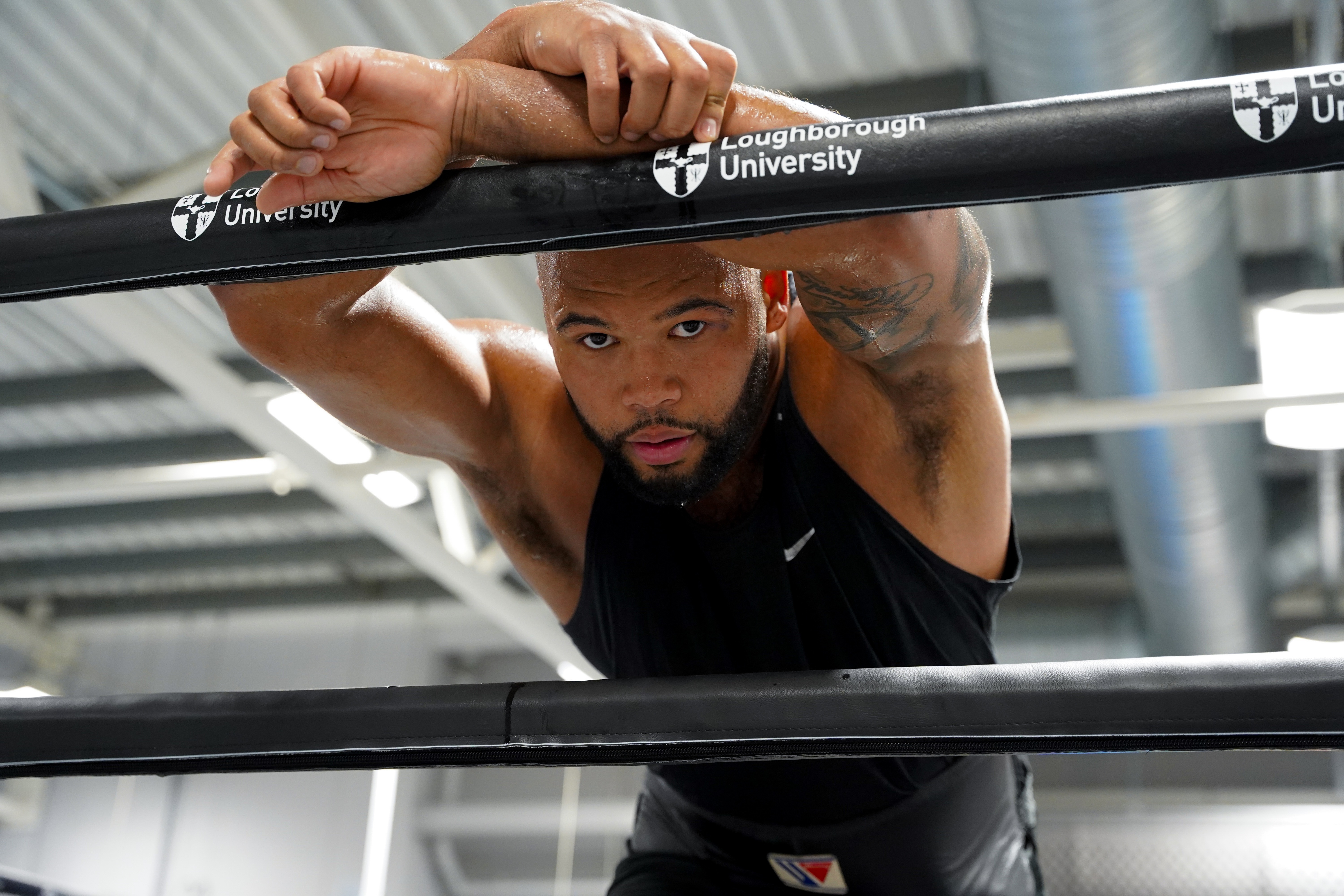 A man with a beard doing chin-ups on a bar bearing the Loughborough University logo.