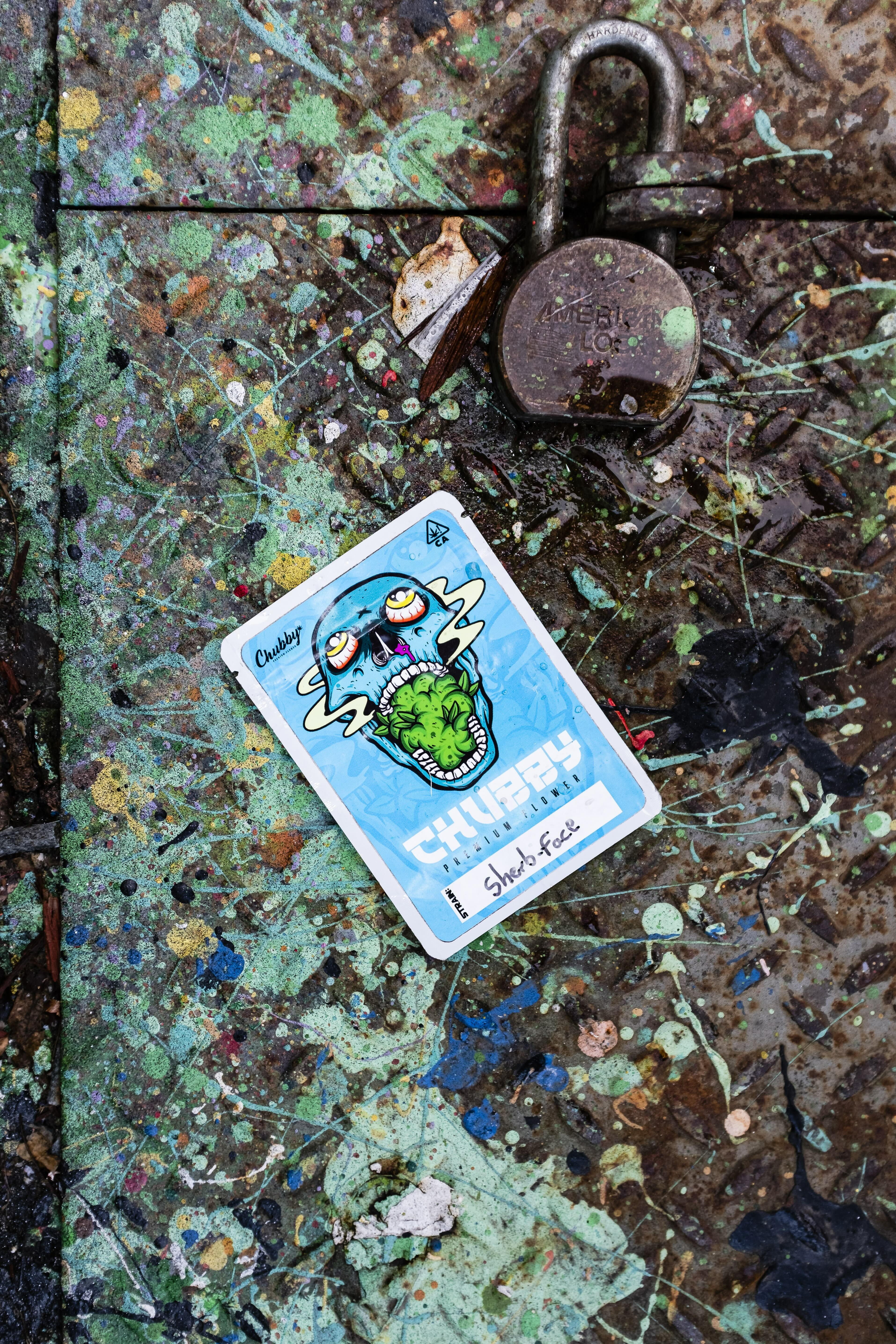 Old padlock and colourful Cheeky trading card on grungy, multi-coloured surface