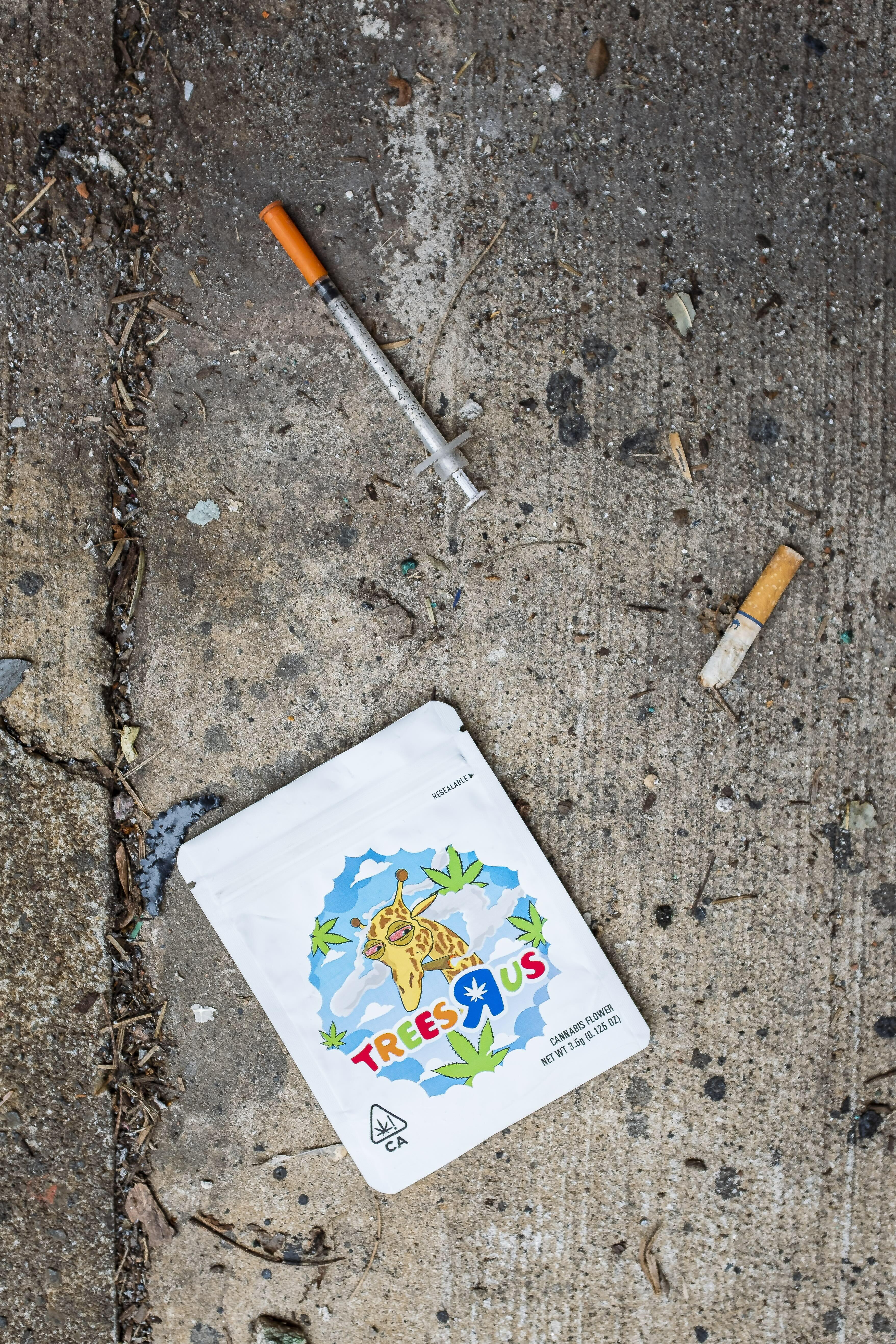 Trees Us logo card on earthy ground, surrounded by drug paraphernalia.