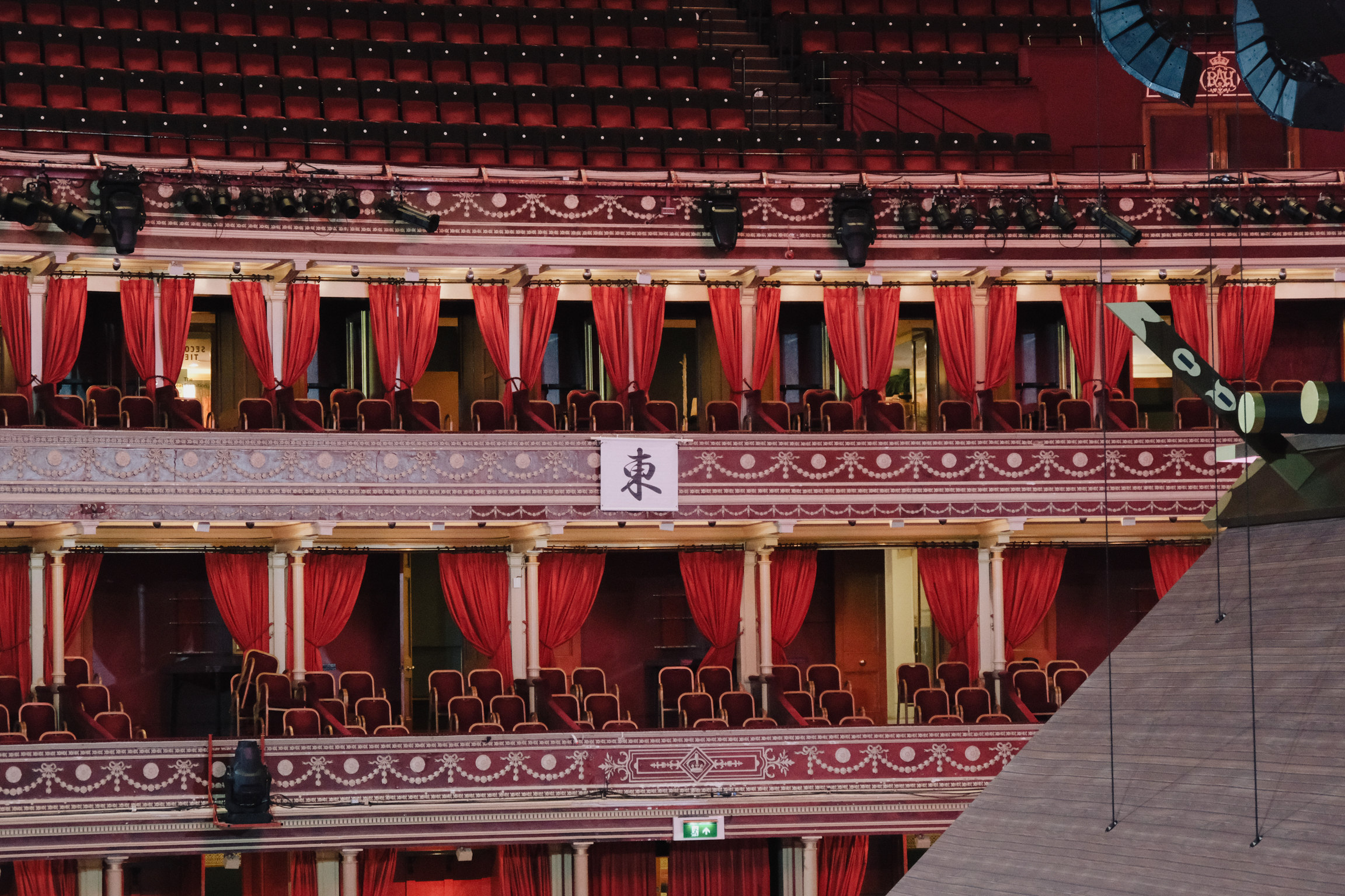 Theatre interior showing three tiers of red velvet curtained boxes with ornate gold decorative trim and burgundy seating.