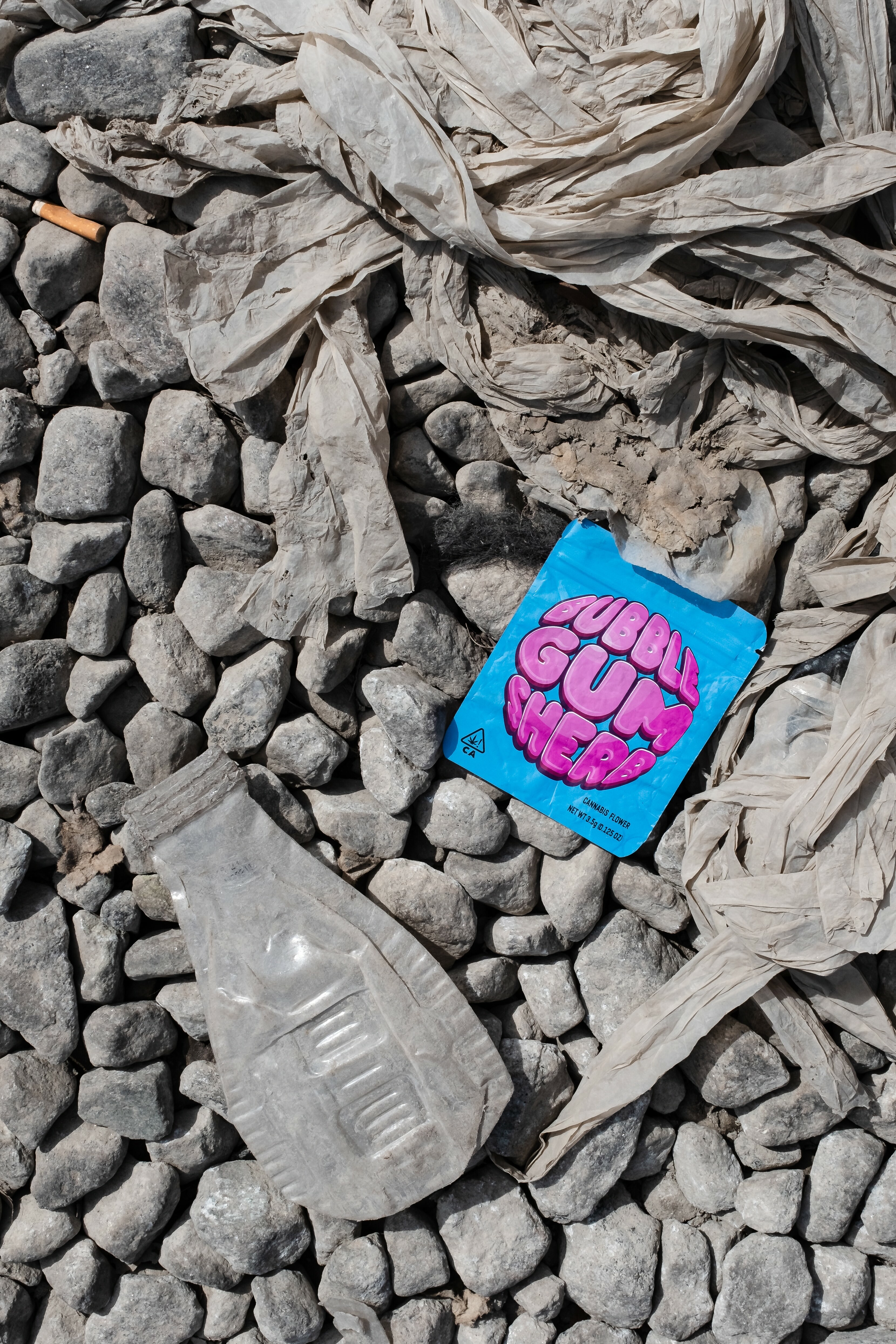 Discarded items on rocky ground, including a blue and pink graphic object and crumpled paper.