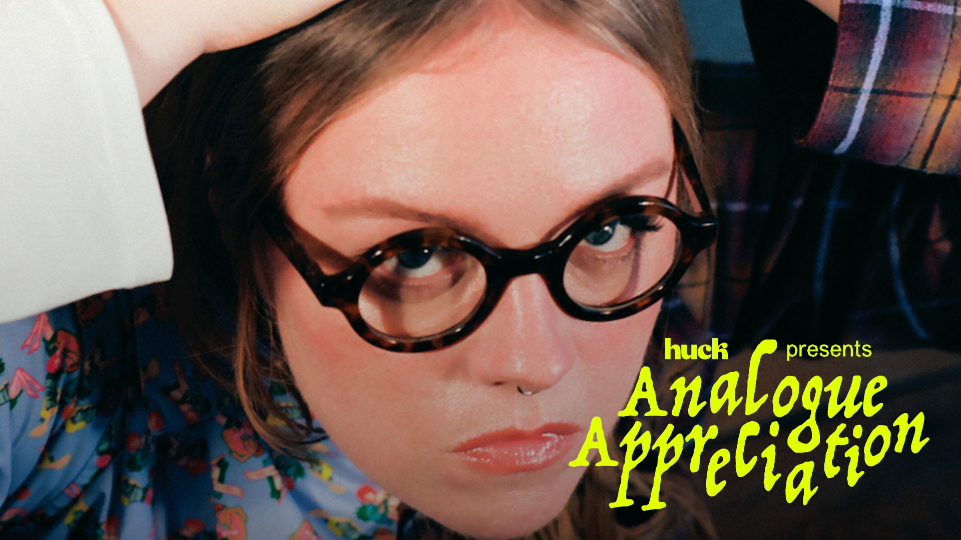 Close-up of woman wearing black-framed glasses against colourful background with 'Huch presents: Analogue Appreciation' text.