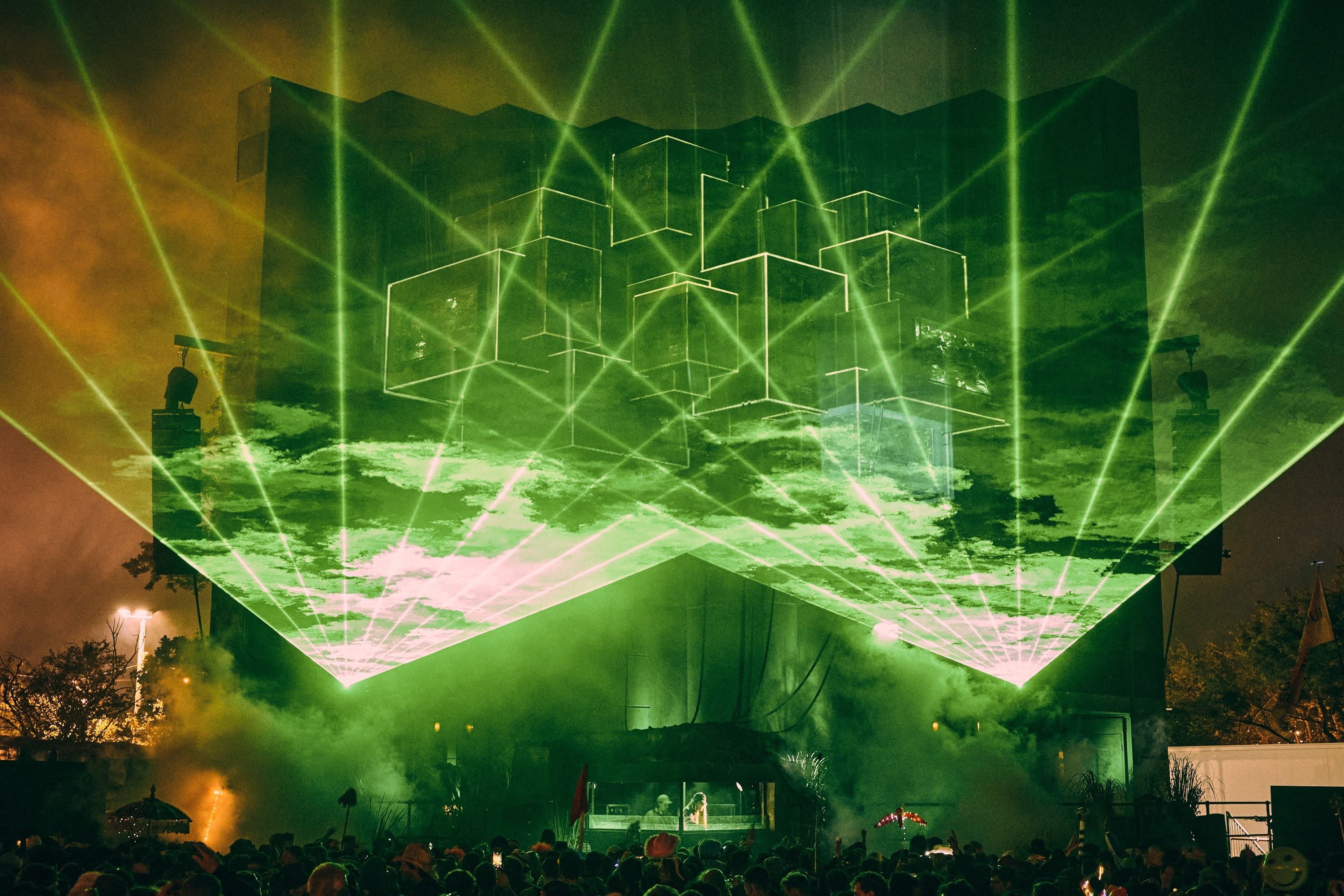 Vast green laser grid projecting onto outdoor stage, with silhouetted figures in foreground.