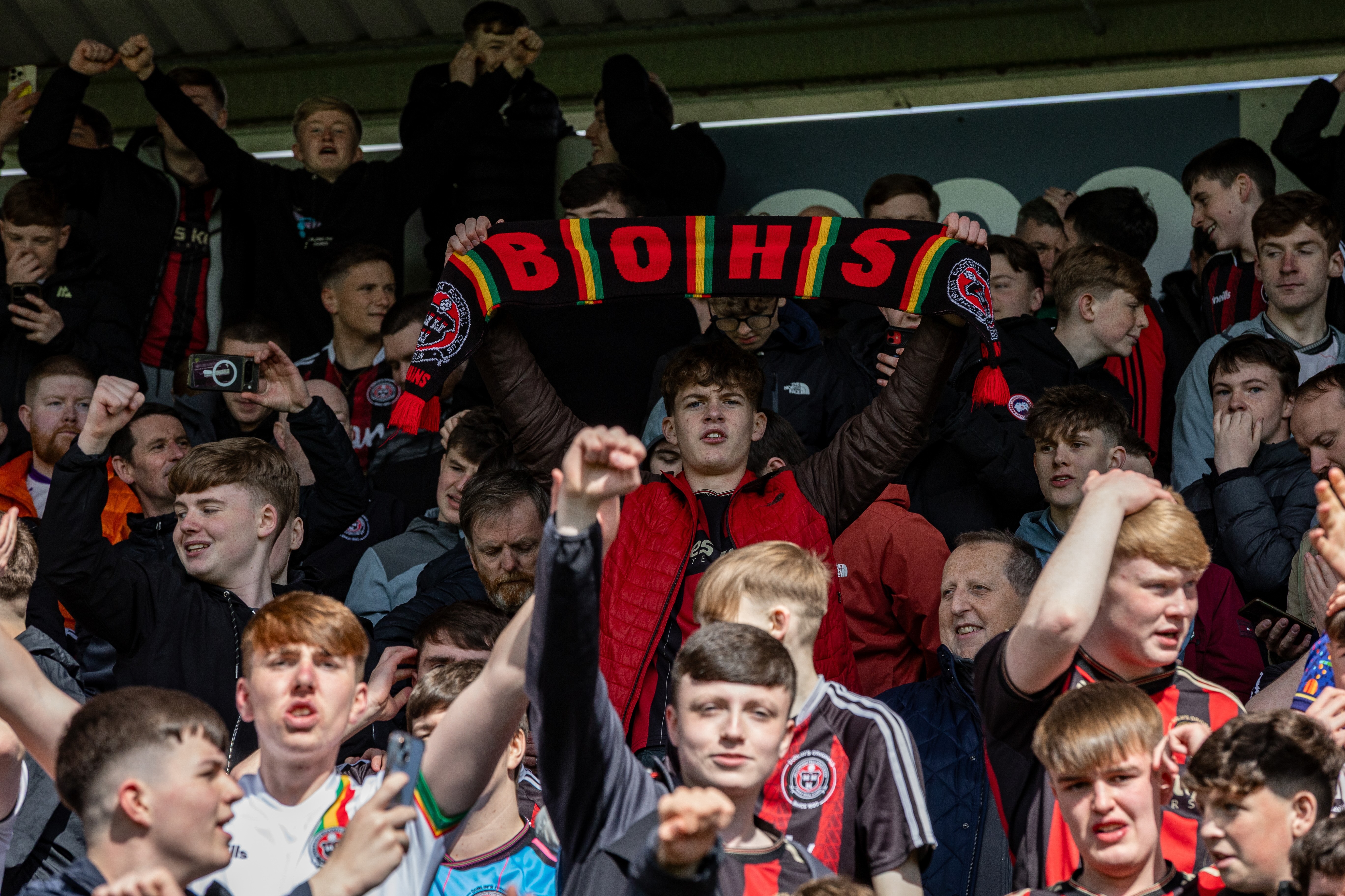 Enthusiastic crowd of football supporters holding up banners and cheering.
