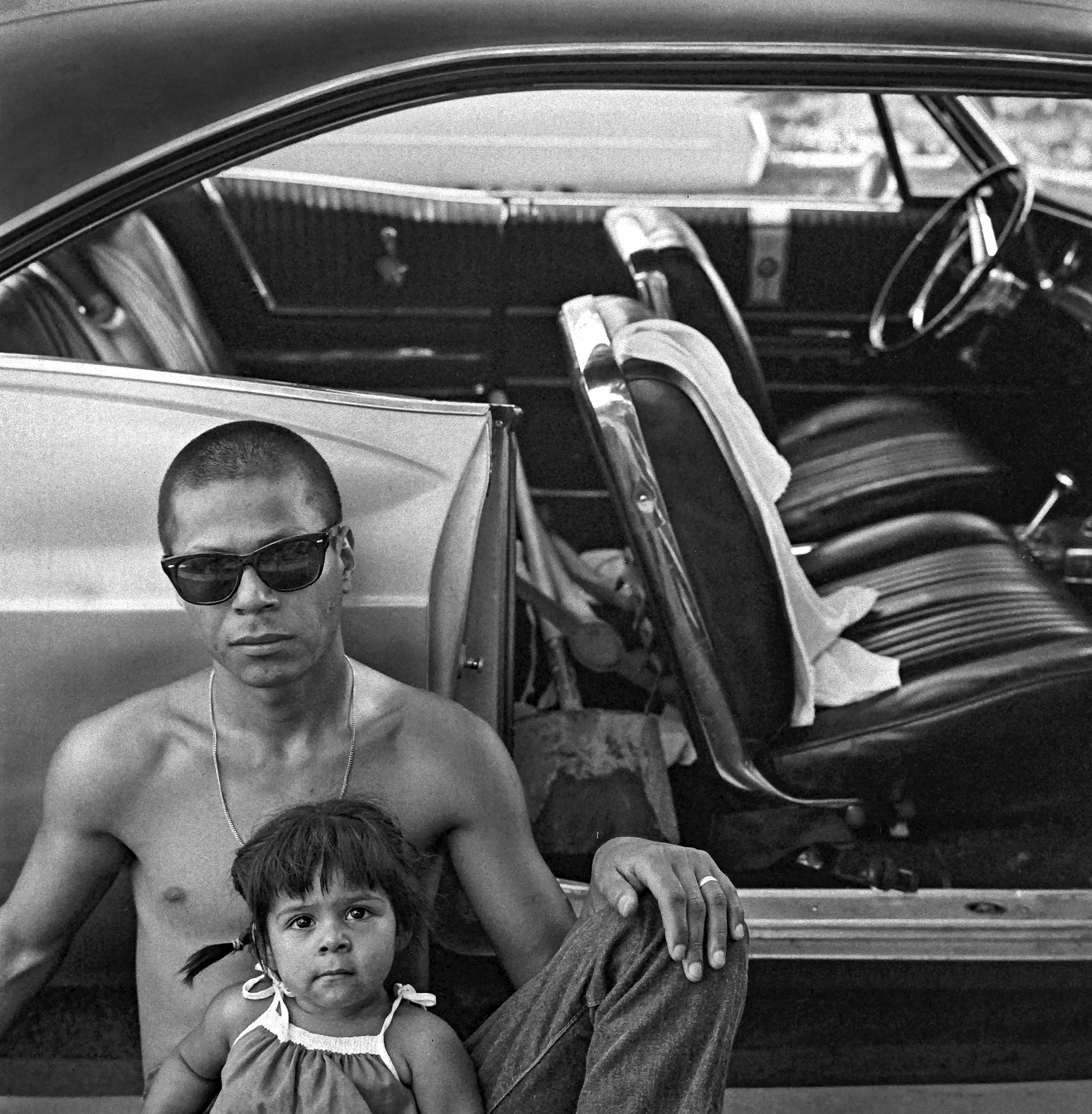 Monochrome image of man and child seated in car interior, angular composition, focus on details of vehicle dashboard and seats.
