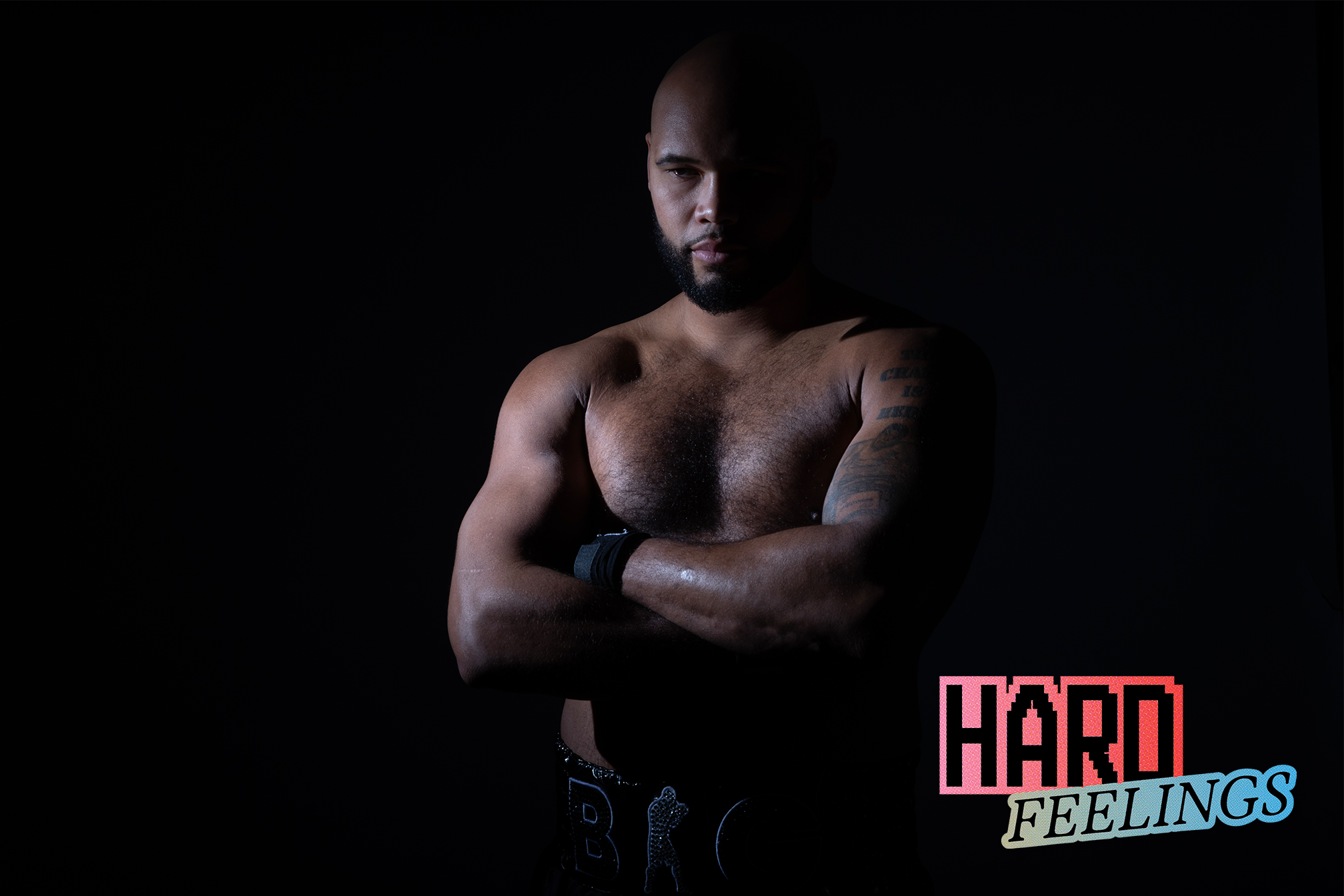 Muscular man with arms crossed in a dark setting, 'Hard Feelings' text overlay.