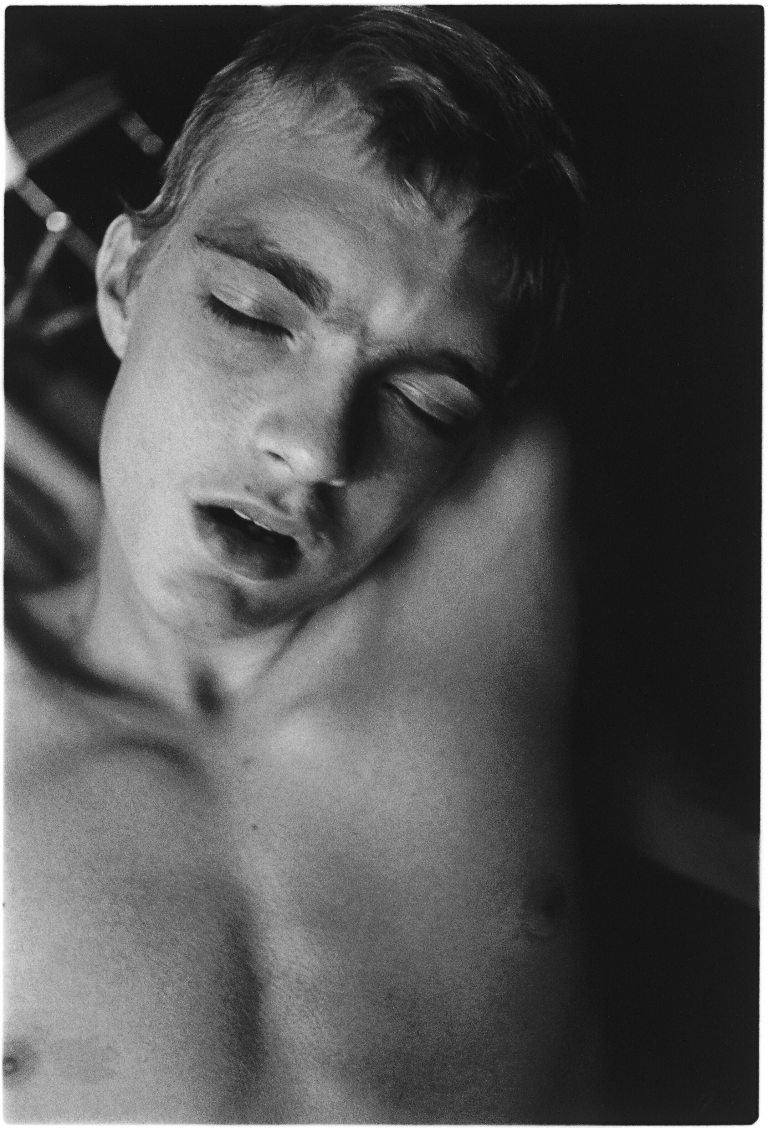 Black and white portrait of person with closed eyes, head tilted back, mouth slightly open, hair swept back.