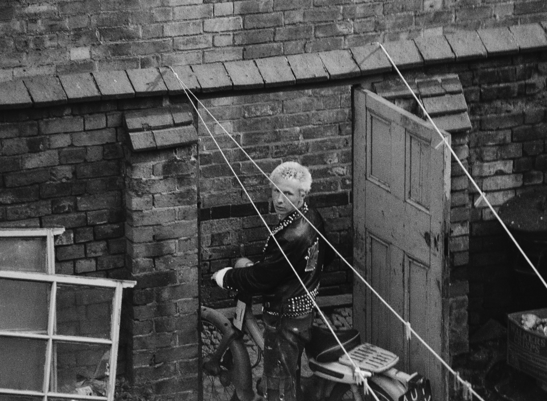 Black and white image showing person in helmet rappelling down brick building wall with ropes, wooden door and window visible.