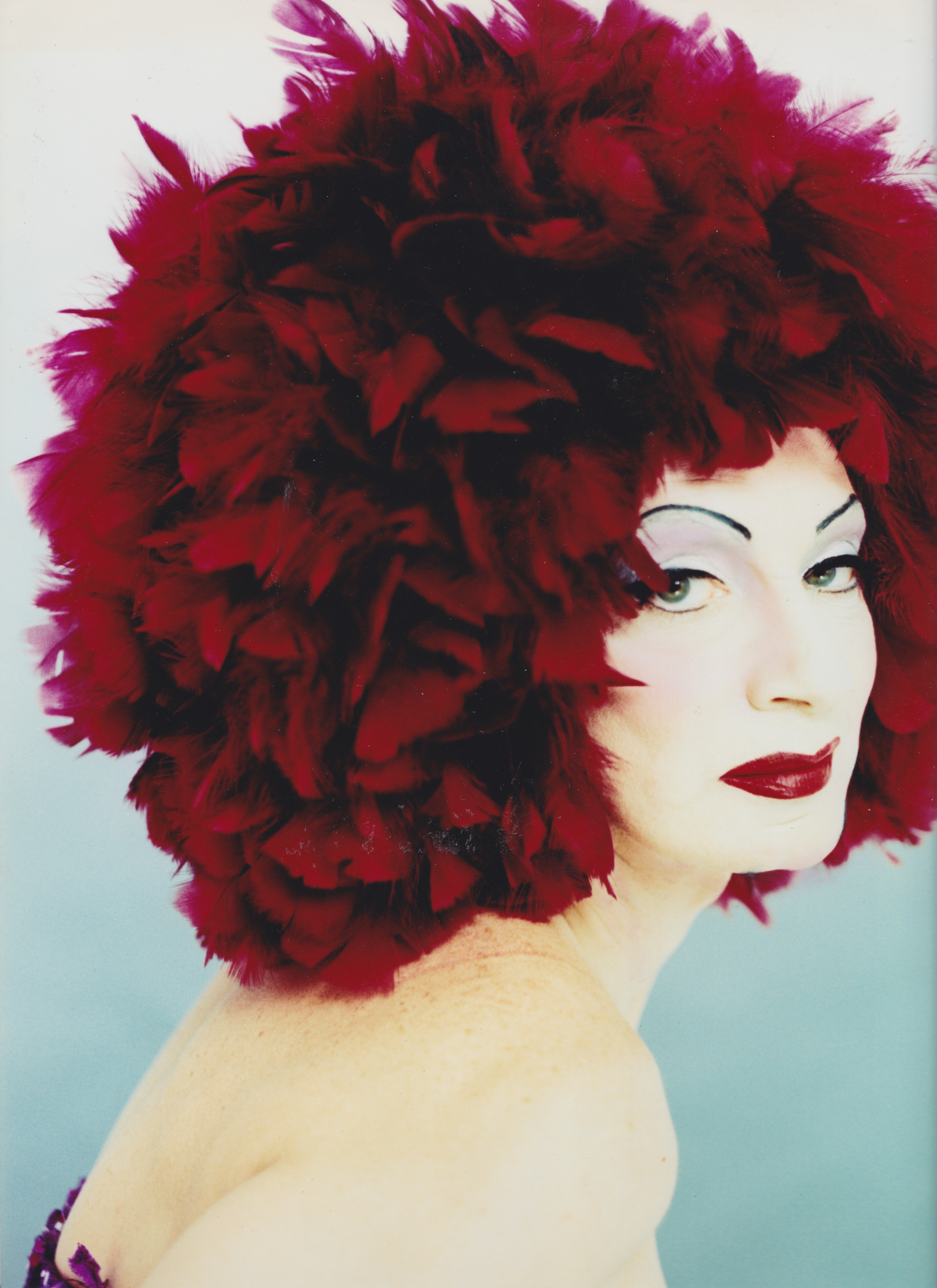 Vibrant red and black feathered headdress, dramatic makeup, thoughtful expression.