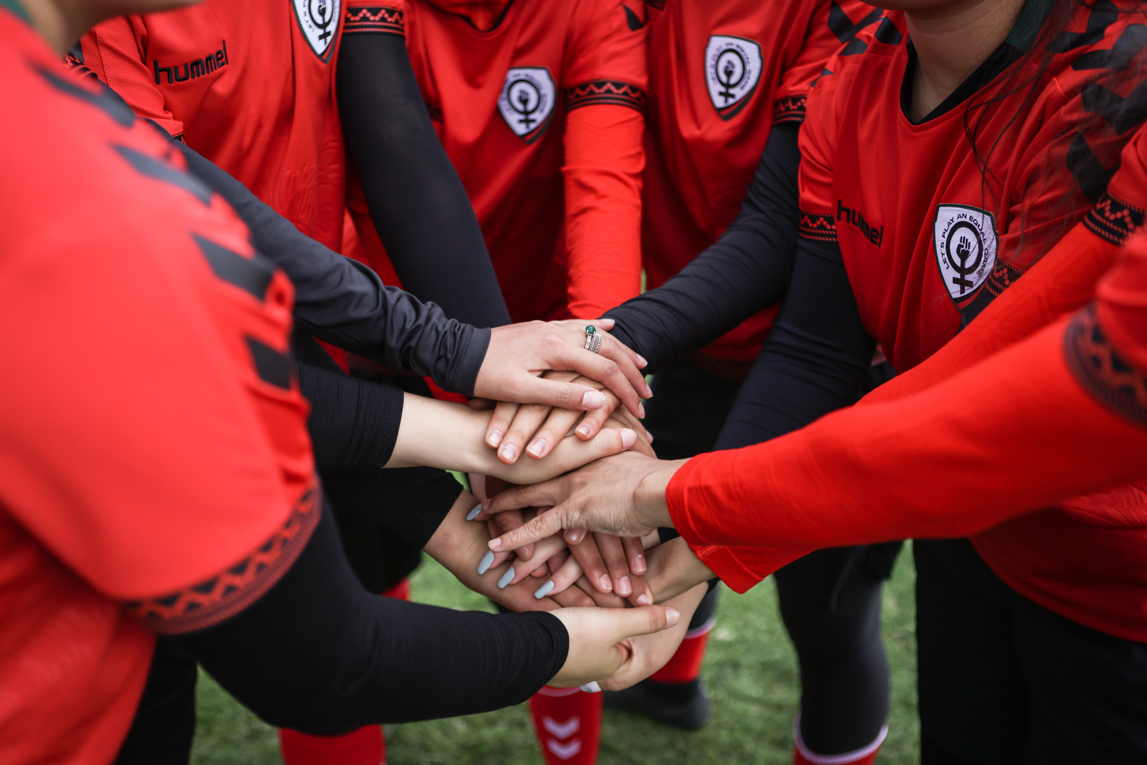 Football players in red and black kit with team badges forming huddle with hands stacked together in centre.