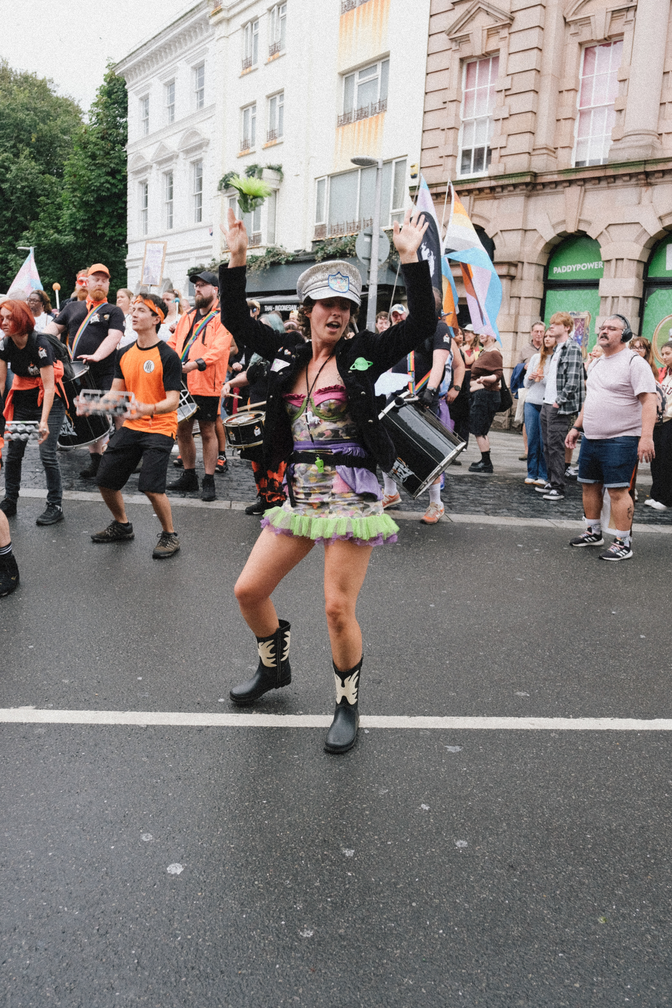 Woman in pirate costume with black hat and colourful skirt dancing in street parade, crowd and Georgian buildings behind