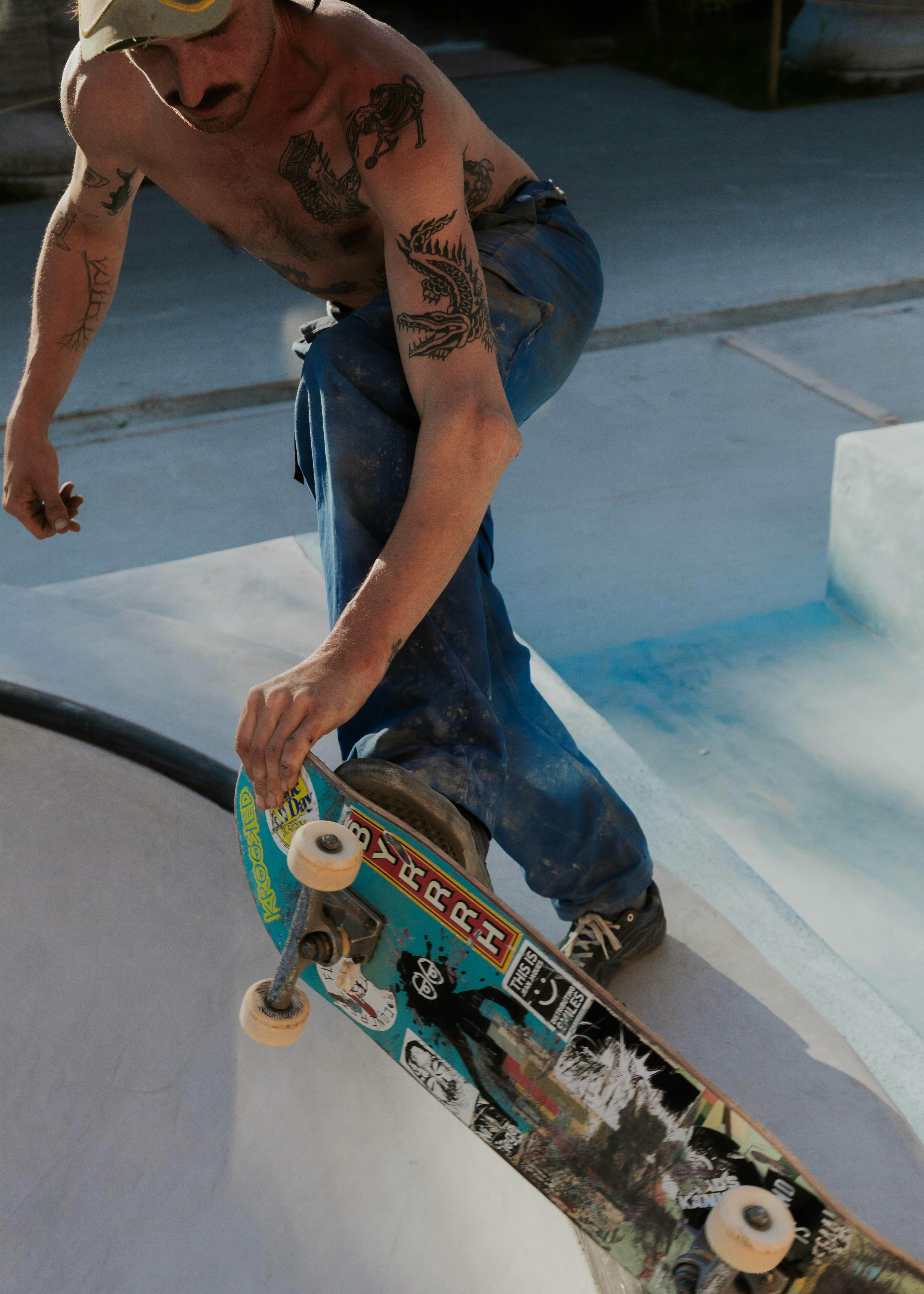 Tattooed person holding a colourful skateboard with stickers and graffiti-style artwork.