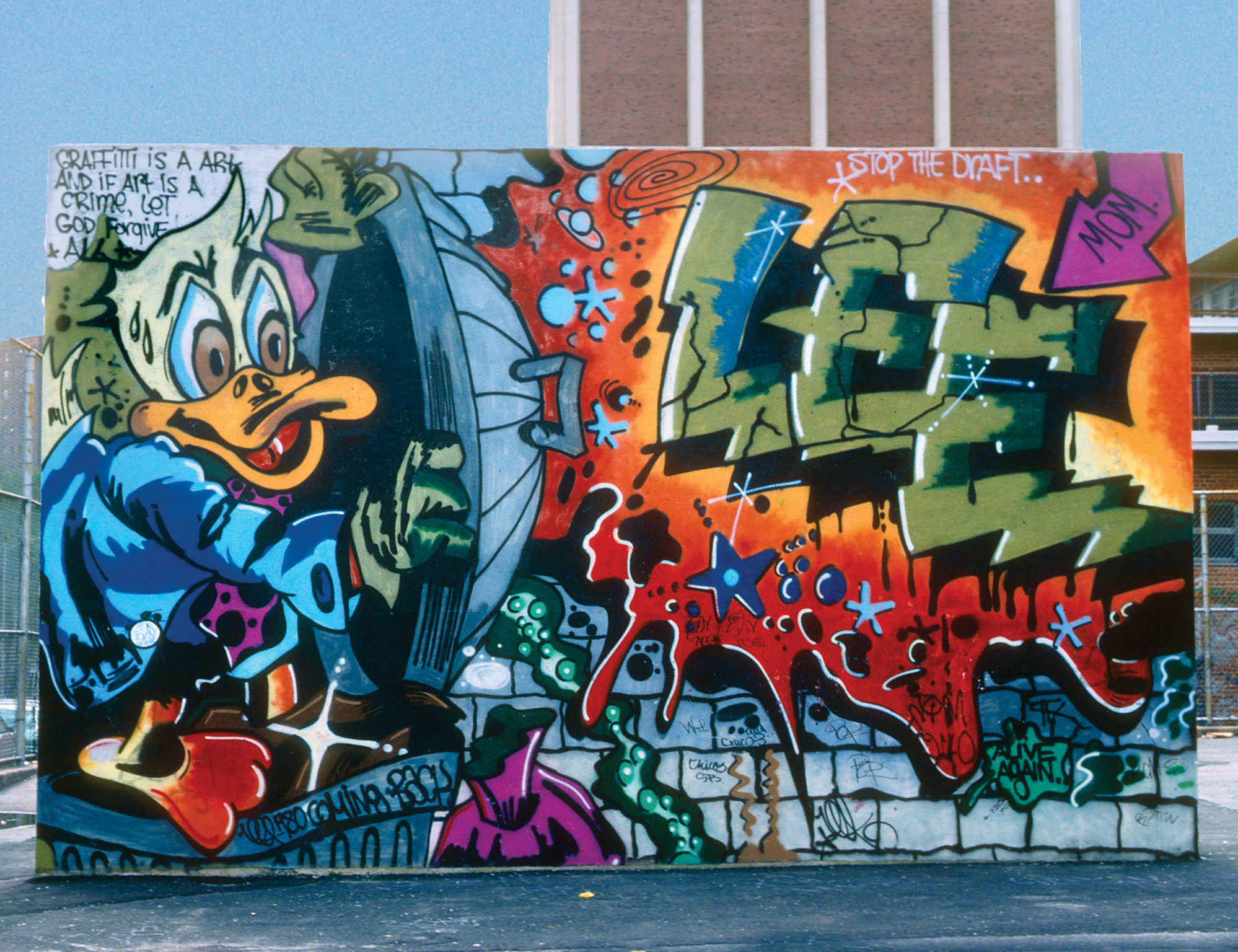 Colourful graffiti mural on brick wall featuring cartoon duck character in blue jacket, orange and green geometric shapes, red lettering.