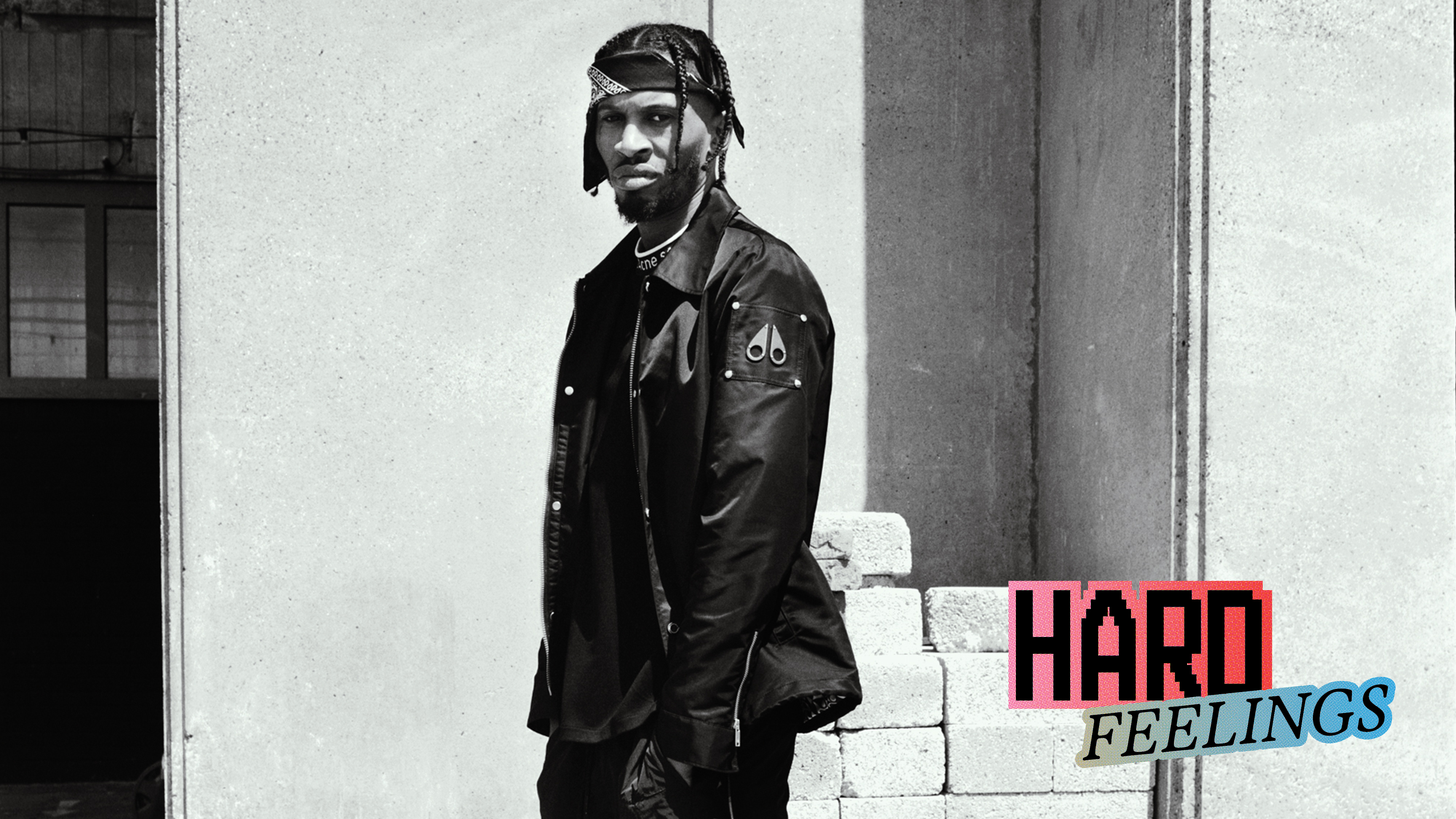 Black and white image of man in leather jacket and cap against concrete wall. Red and blue text reading "HARD FEELINGS" in bottom right.