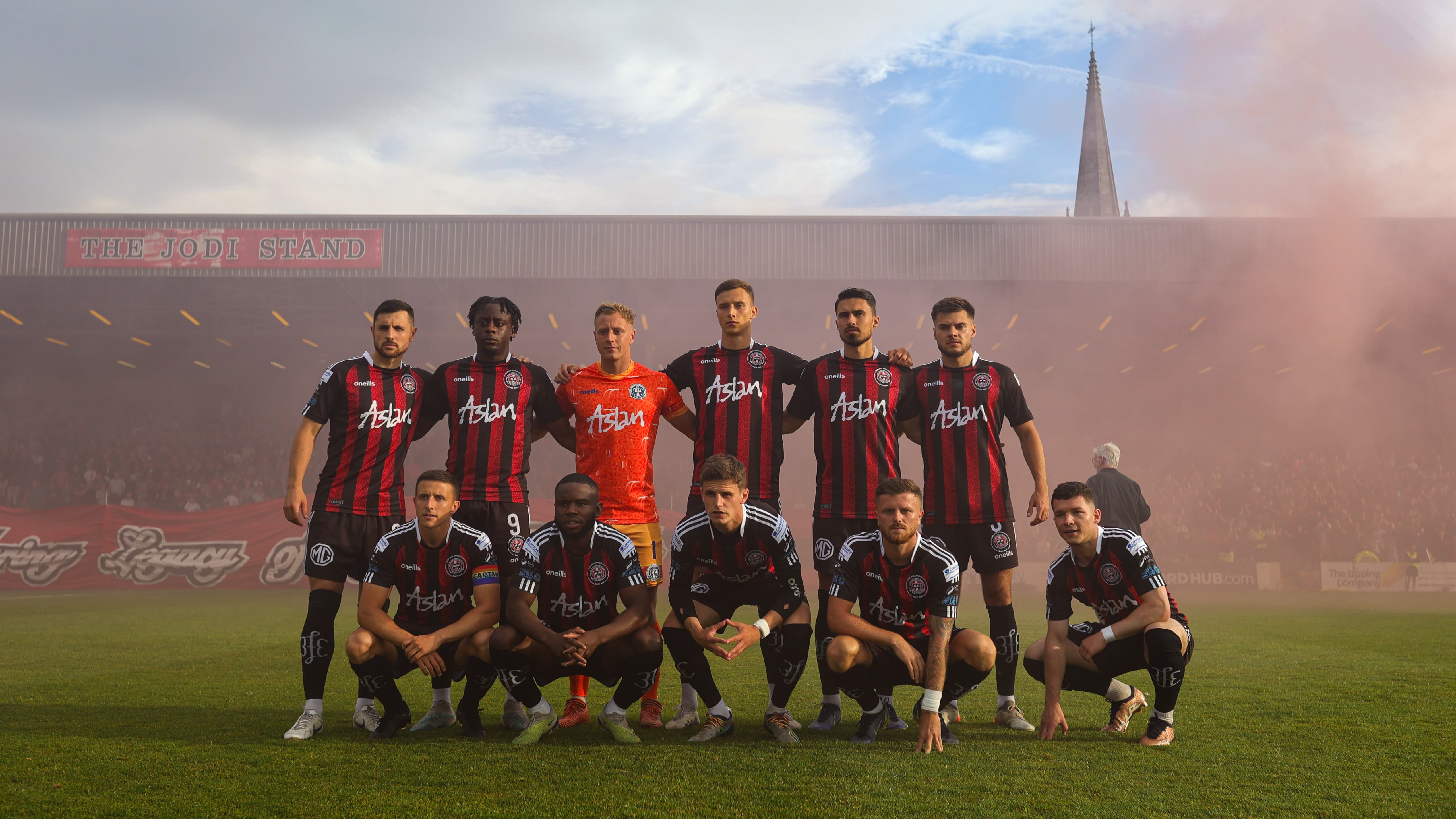 Football team in red and black uniforms posing on a pitch.
