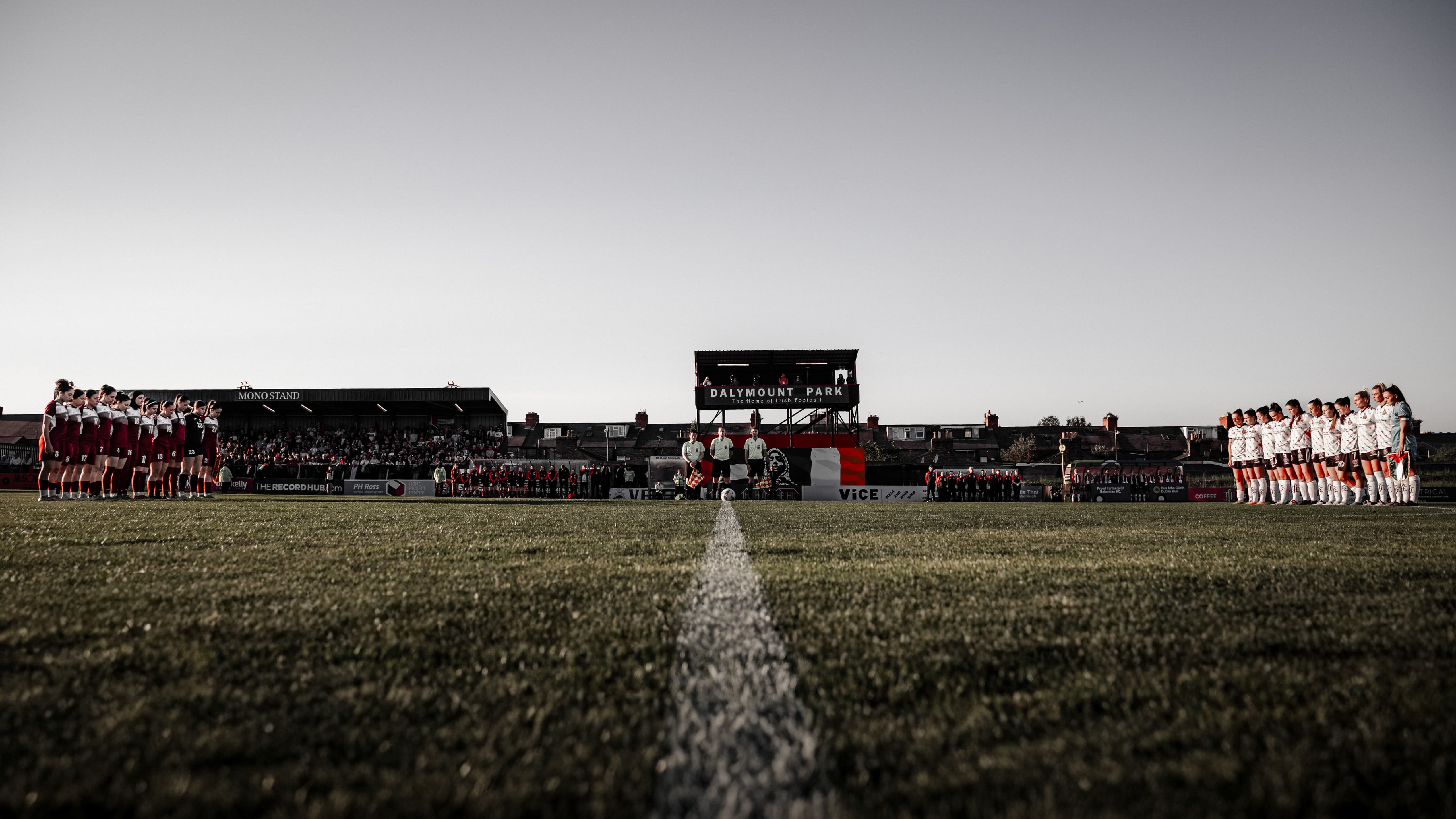 Two teams on a sports field, fans in the stands, scoreboard visible.
