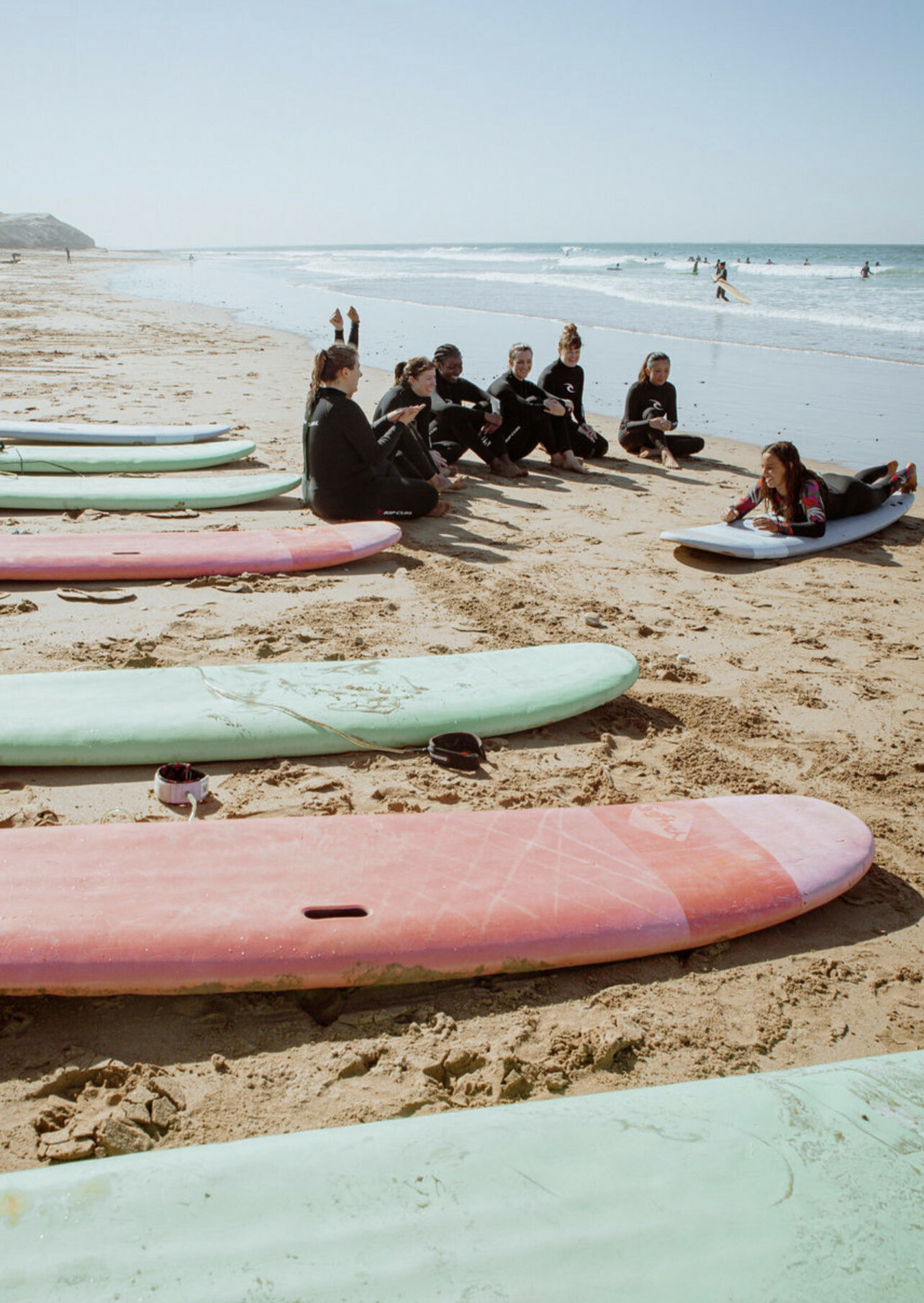 Colourful surfboards on beach, people learning to surf in the water.