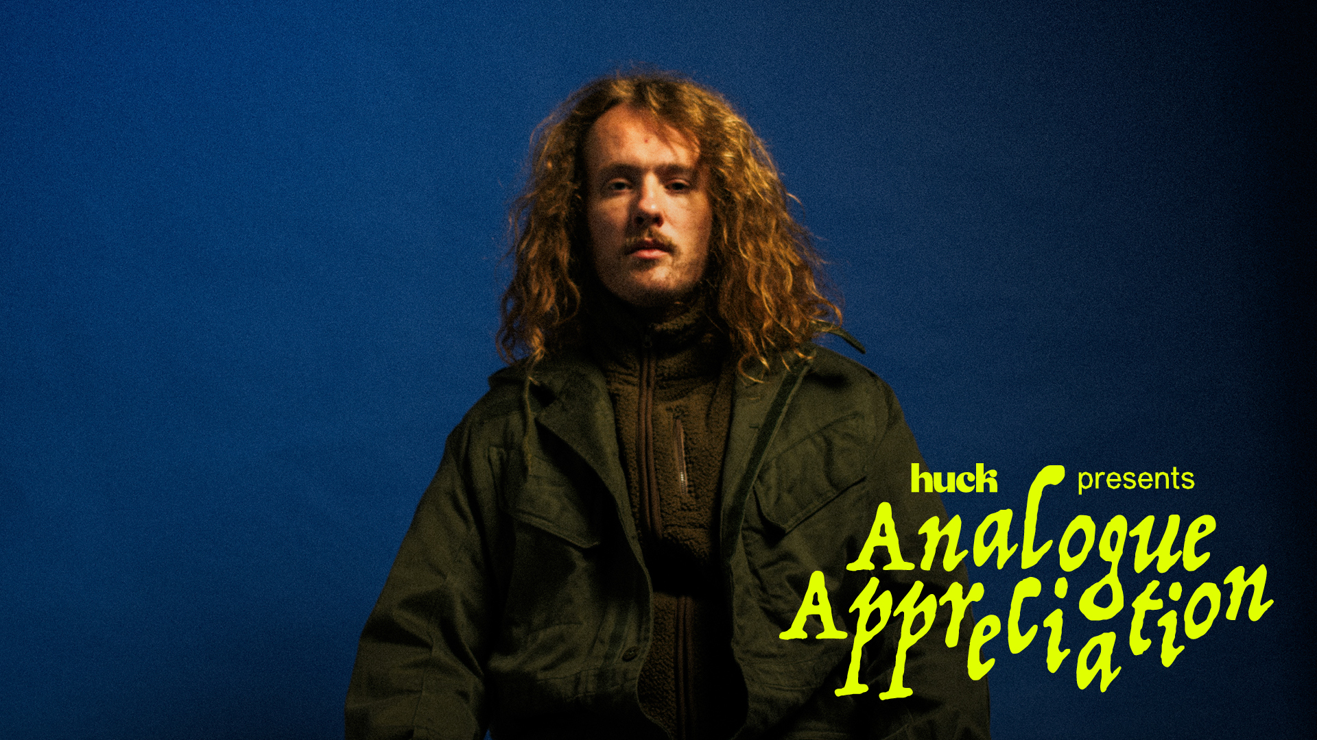 A man with long curly hair and a beard wearing a green jacket against a dark blue background with "Analogue Appreciation" text in yellow.