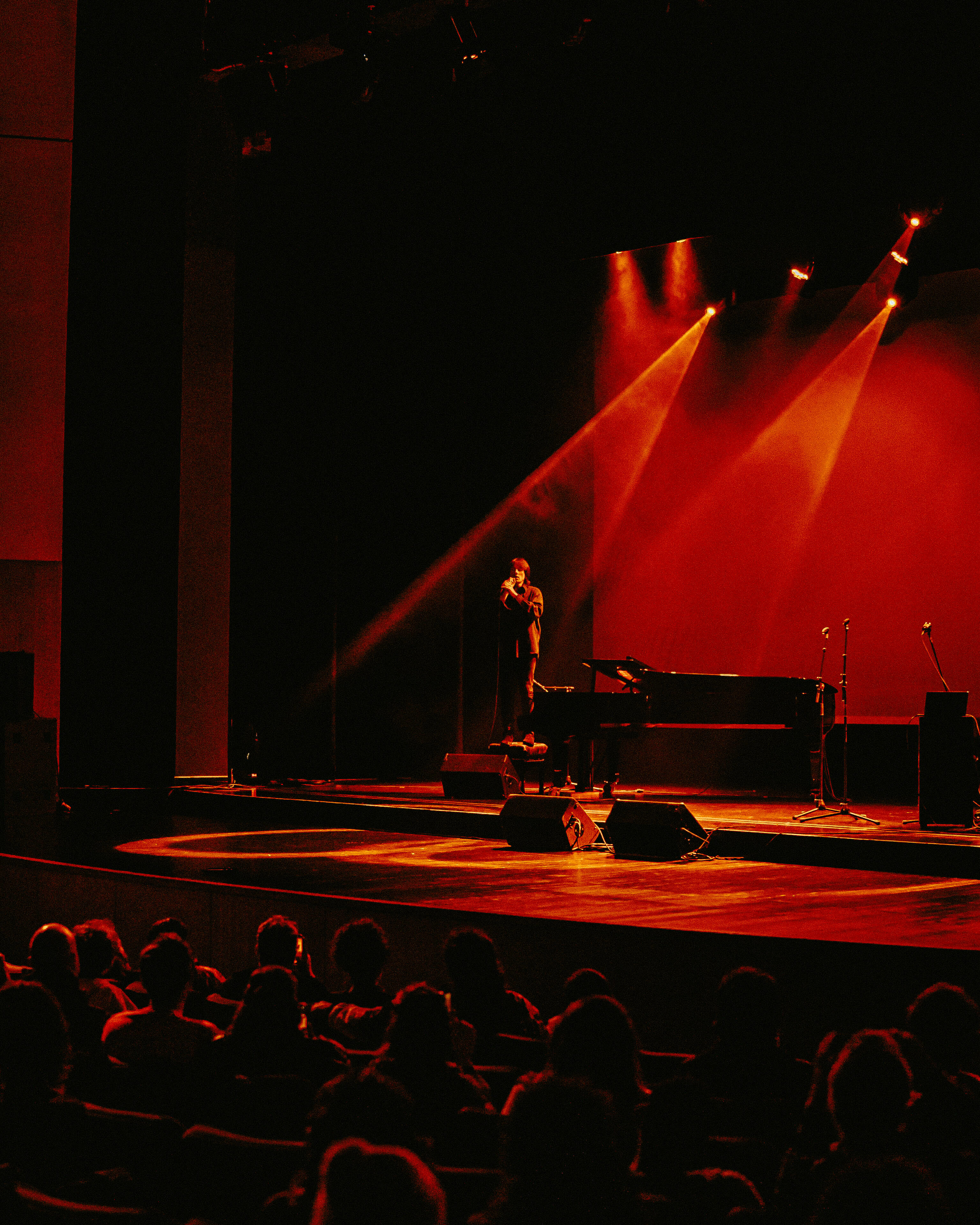 Illuminated stage with piano and spotlight, audience in foreground.
