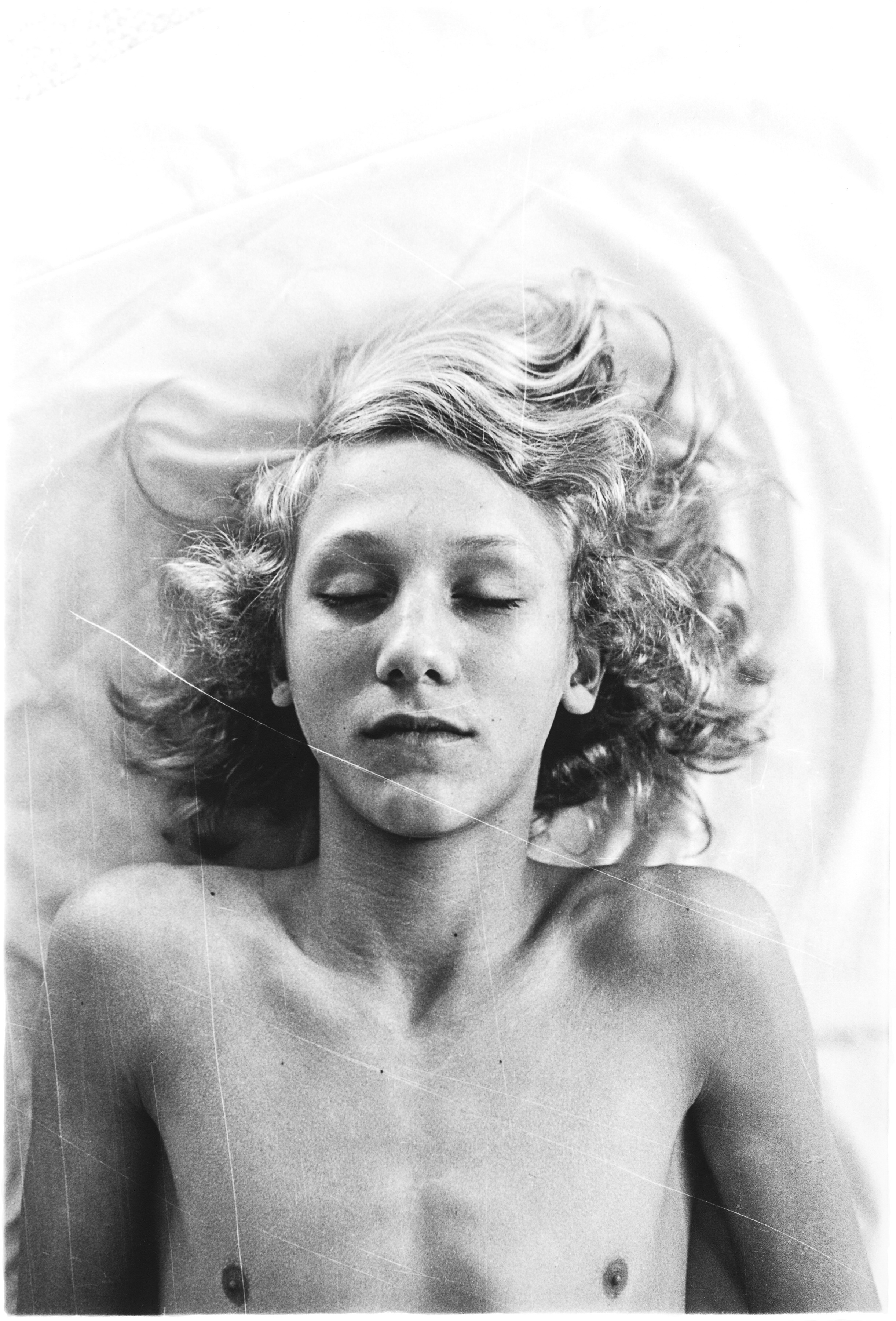 Black and white portrait of woman with closed eyes, wavy hair spread out, upper body visible, soft lighting with dreamy quality.