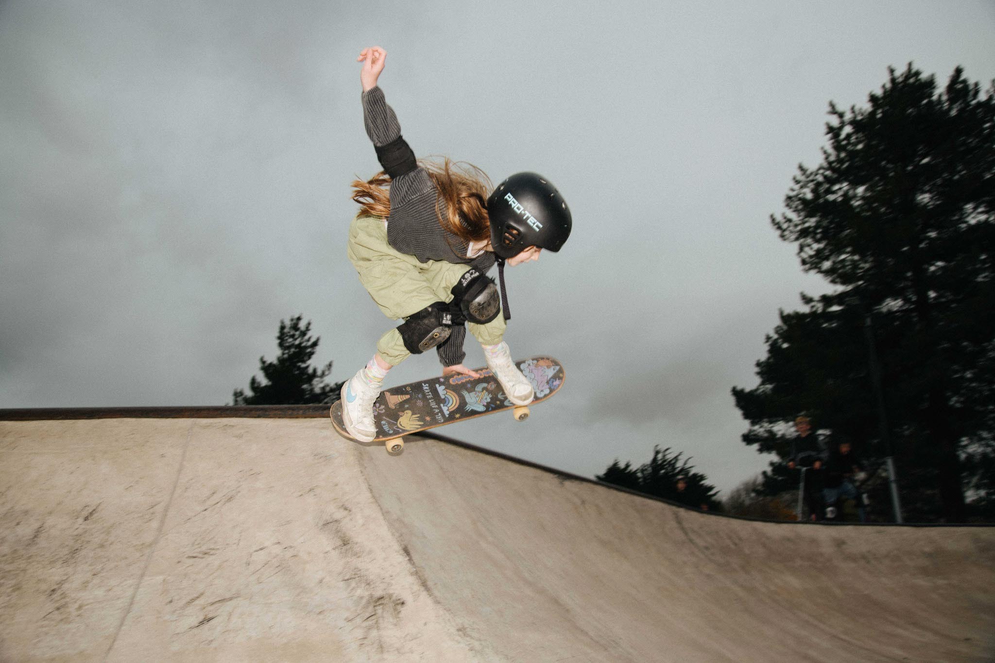 Skater in mid-air performing trick on a ramp, against a cloudy sky background with trees.