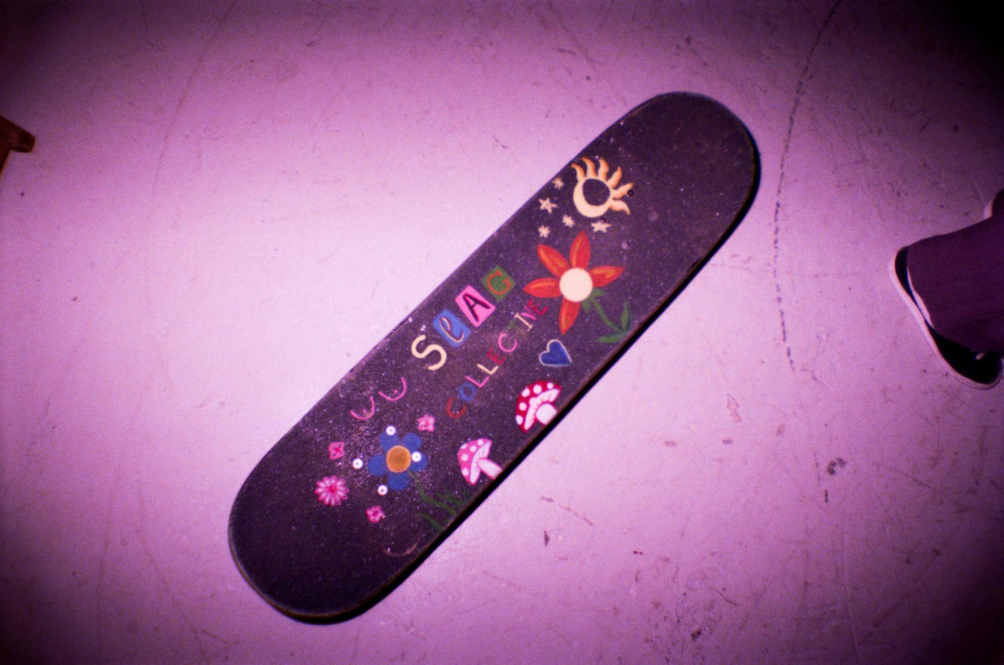 Decorated black skateboard deck with colourful hand-drawn designs including flowers, symbols, and text.