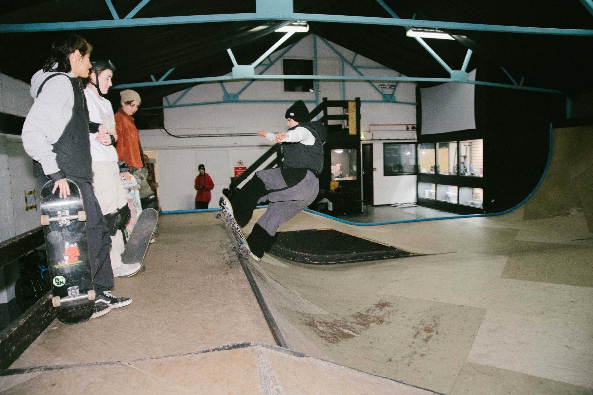 Indoor skate park with ramps, riders, and abstract architectural elements in blue, white, and black tones.