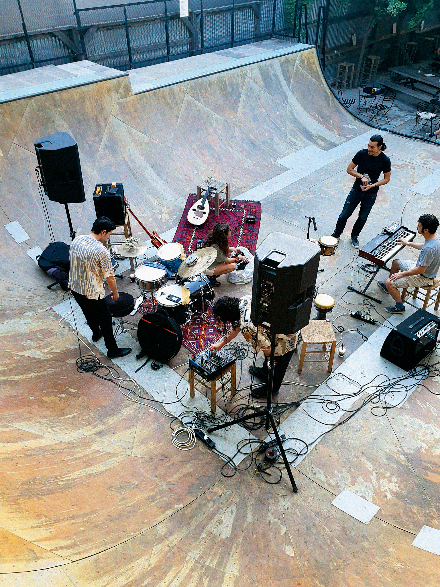 Band performing in empty concrete skate bowl with drums, guitars, amplifiers and microphones set up on red carpet.