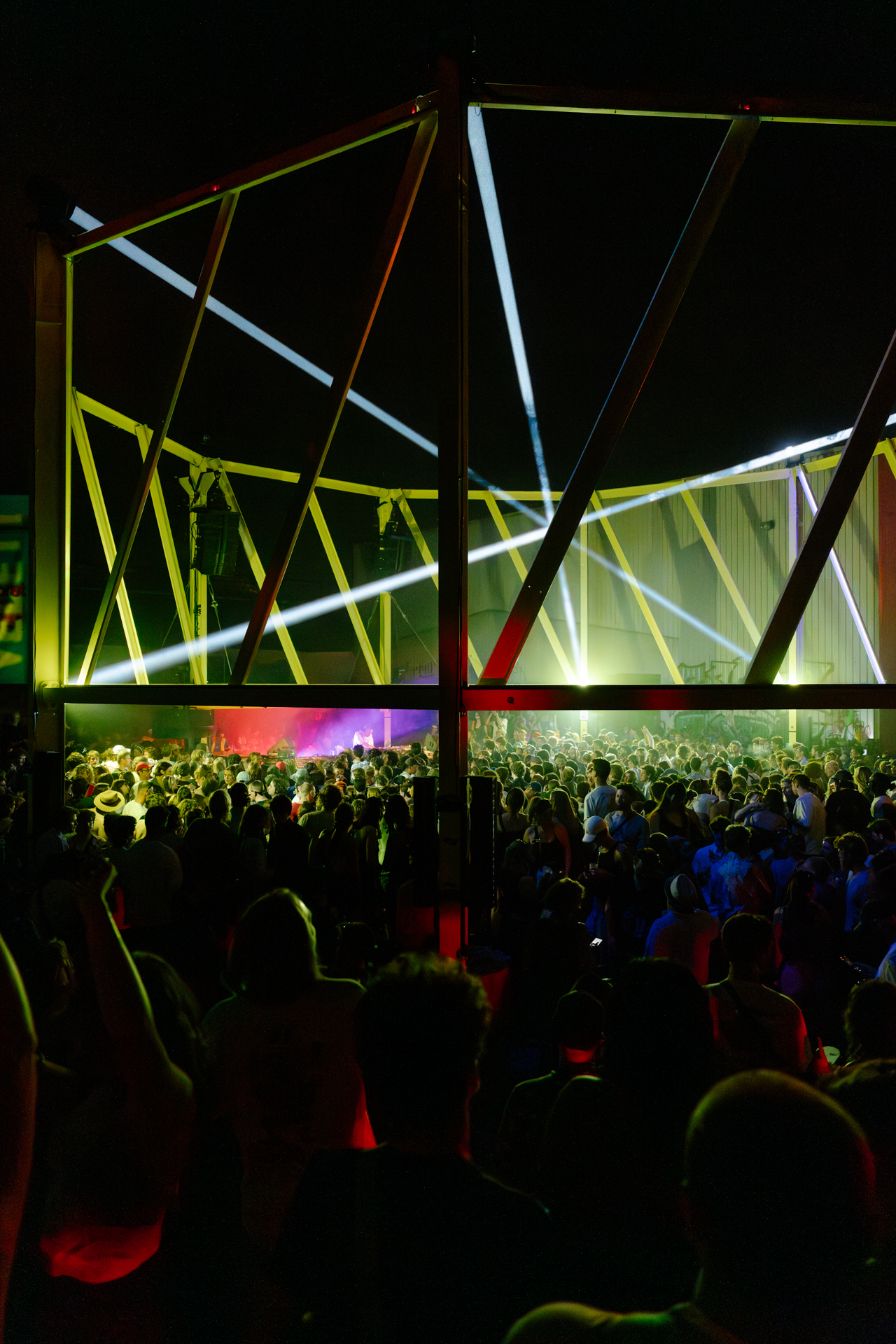Vibrant, geometric lighting frames a crowded nighttime music festival with a large crowd.
