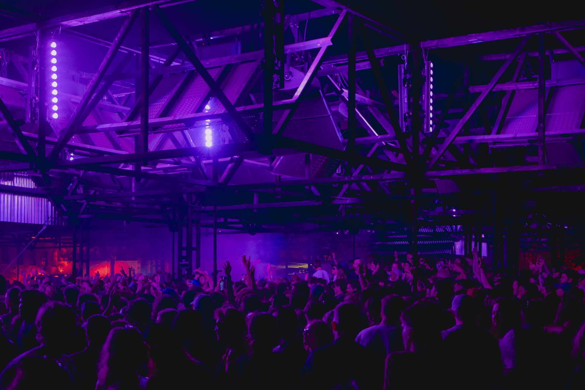 Crowded indoor venue with vibrant purple lighting and silhouetted audience.