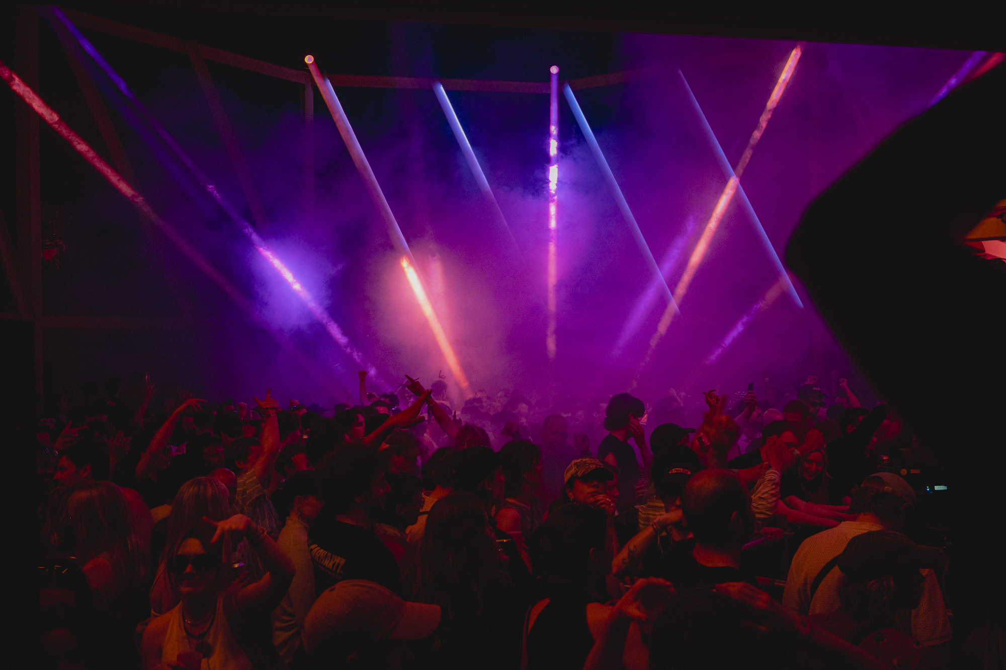 Crowd at a concert with colourful stage lighting and spotlights.
