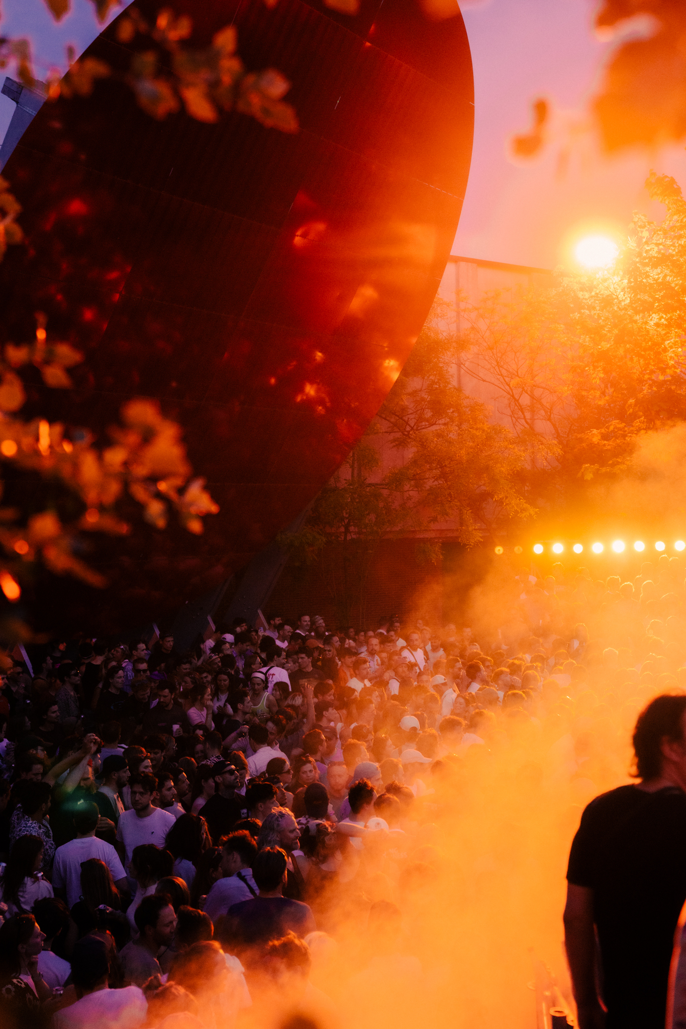 Vibrant crowd at music festival, with warm orange and red lighting illuminating the scene.